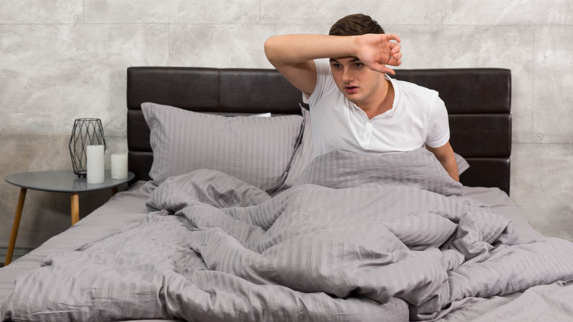 man who's a warm sleeper sitting up in bed feeling hot