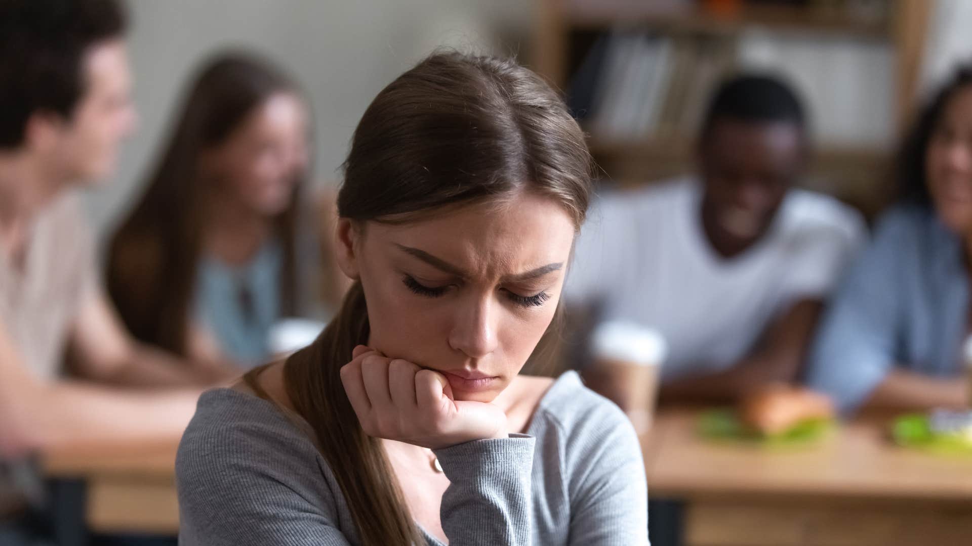 woman feeling sad as people make fun of her behind her