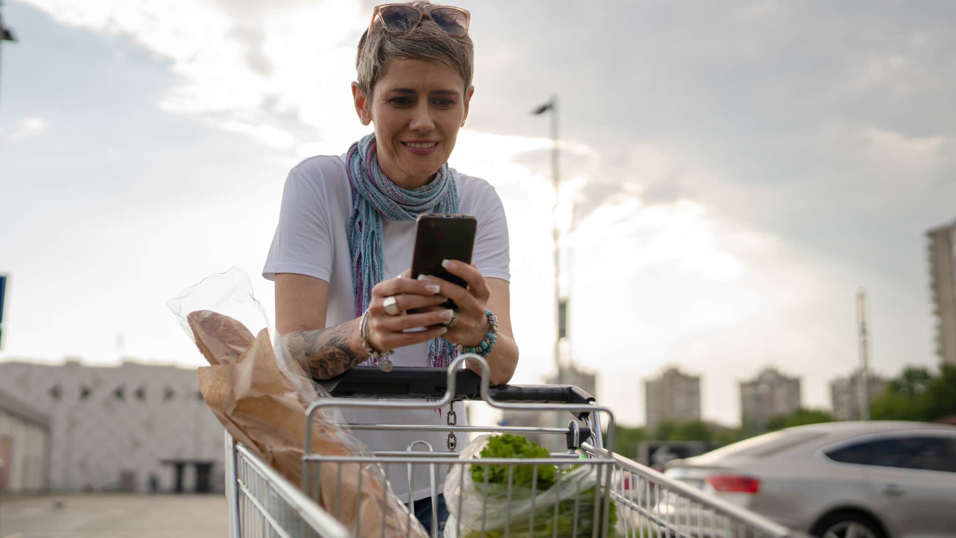 woman texting pushing shopping cart in parking lot