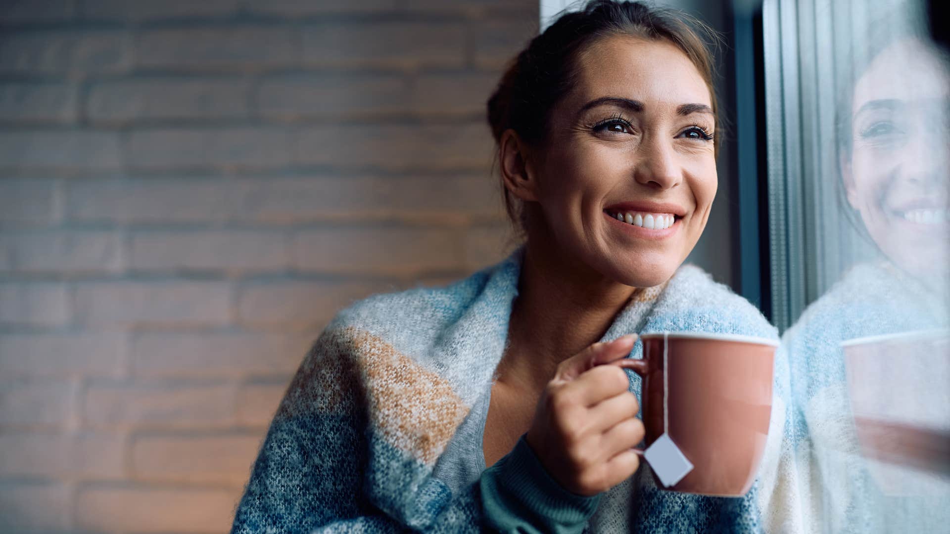 naturally introspective people who prefer tea over coffee usually have these surprisingly grounded personality traits Woman who's naturally introspective drinking tea and smiling.