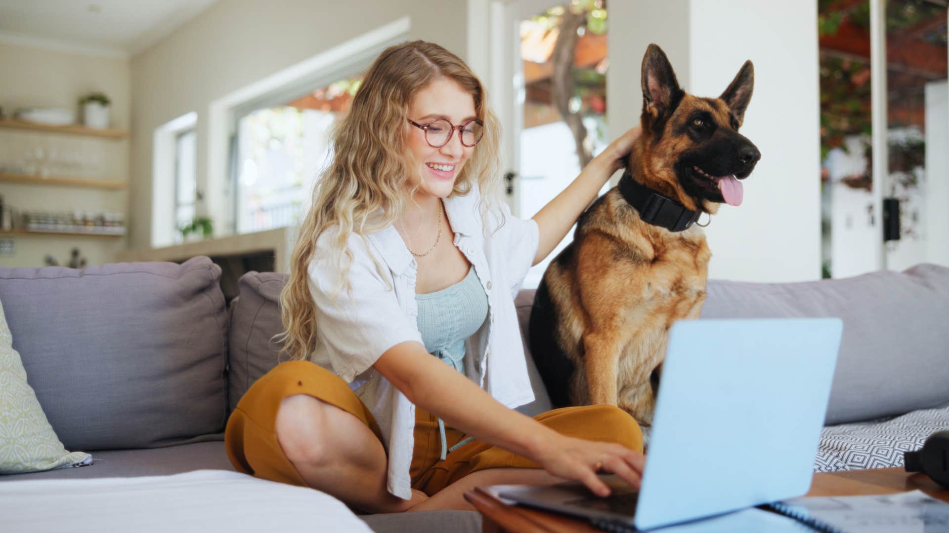woman sitting next to dog while working on laptop