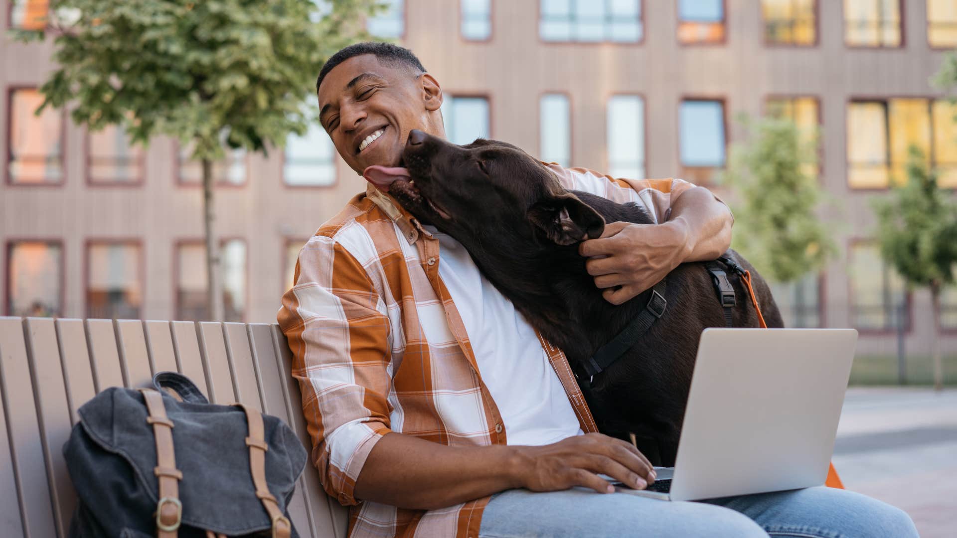 dog licking man's face while sitting on park bench outside