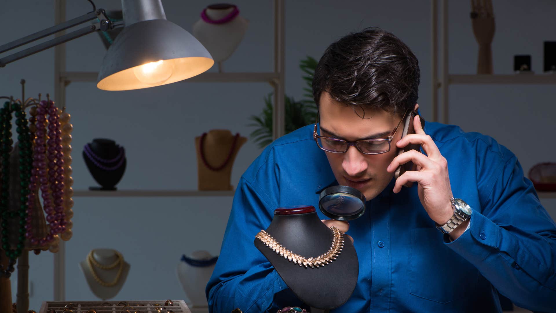 man in dark blue shirt looking at broken jewelry with microscope 