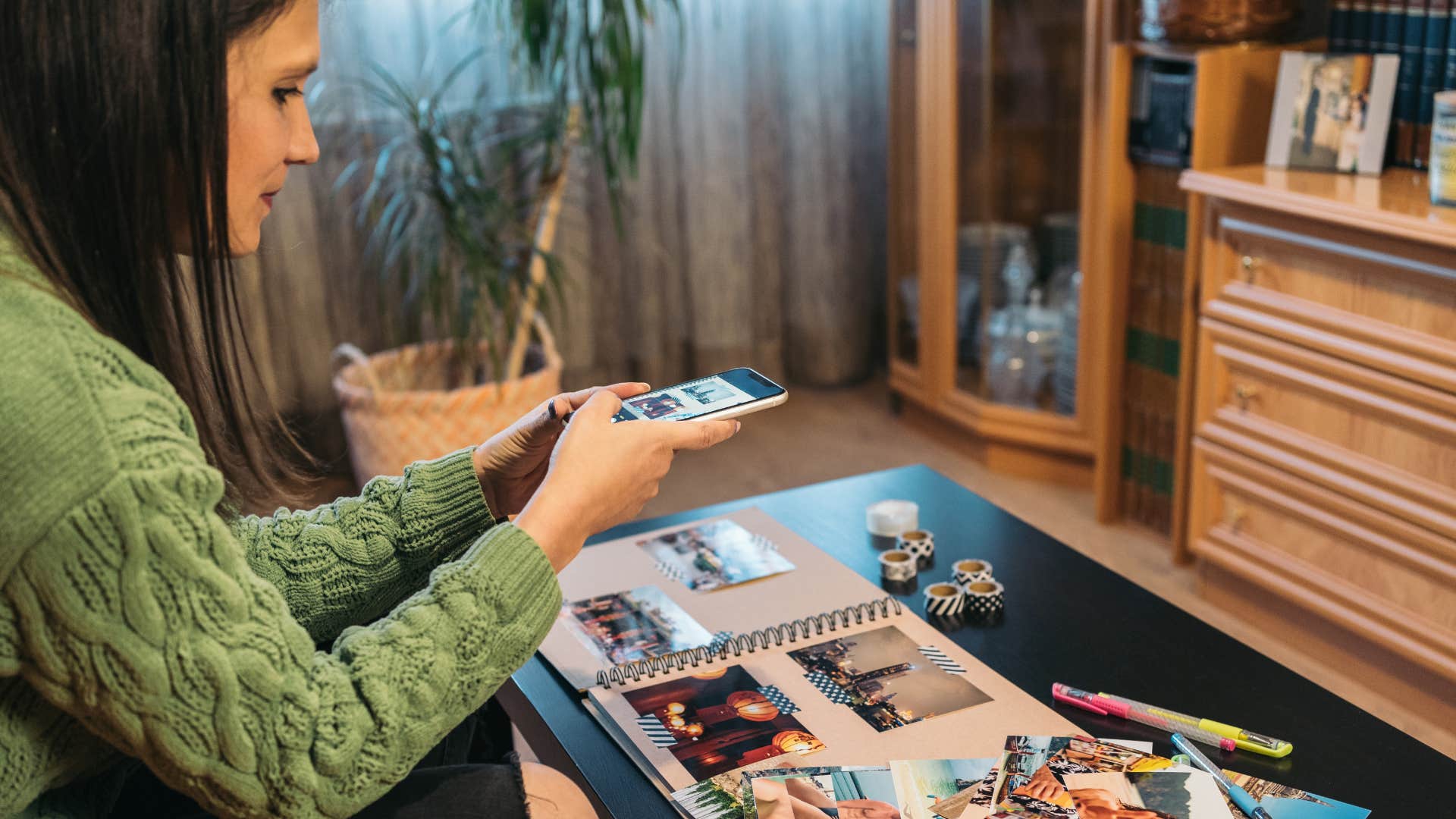 woman in green shirt looking at unlabeled photographs and taking a picture