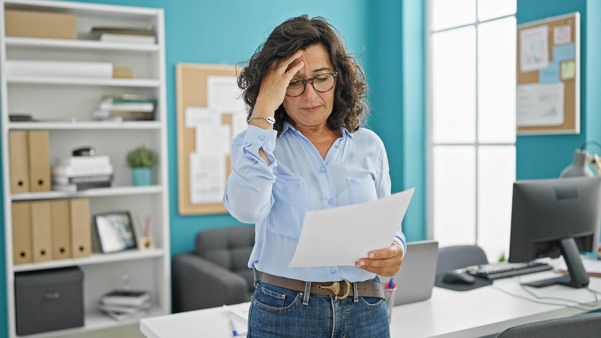 woman in blue shirt looking at unorganized paperwork with frustration