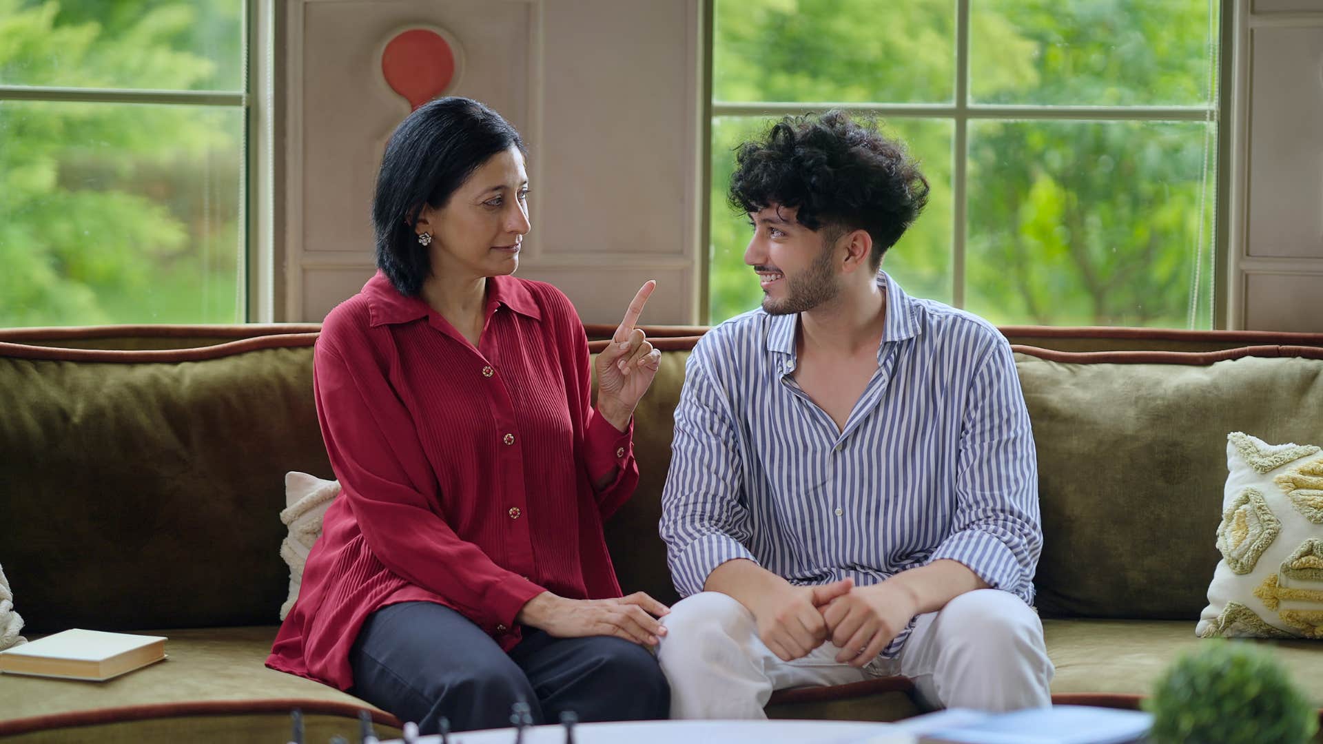  mother with young adult son sitting on cozy couch talking