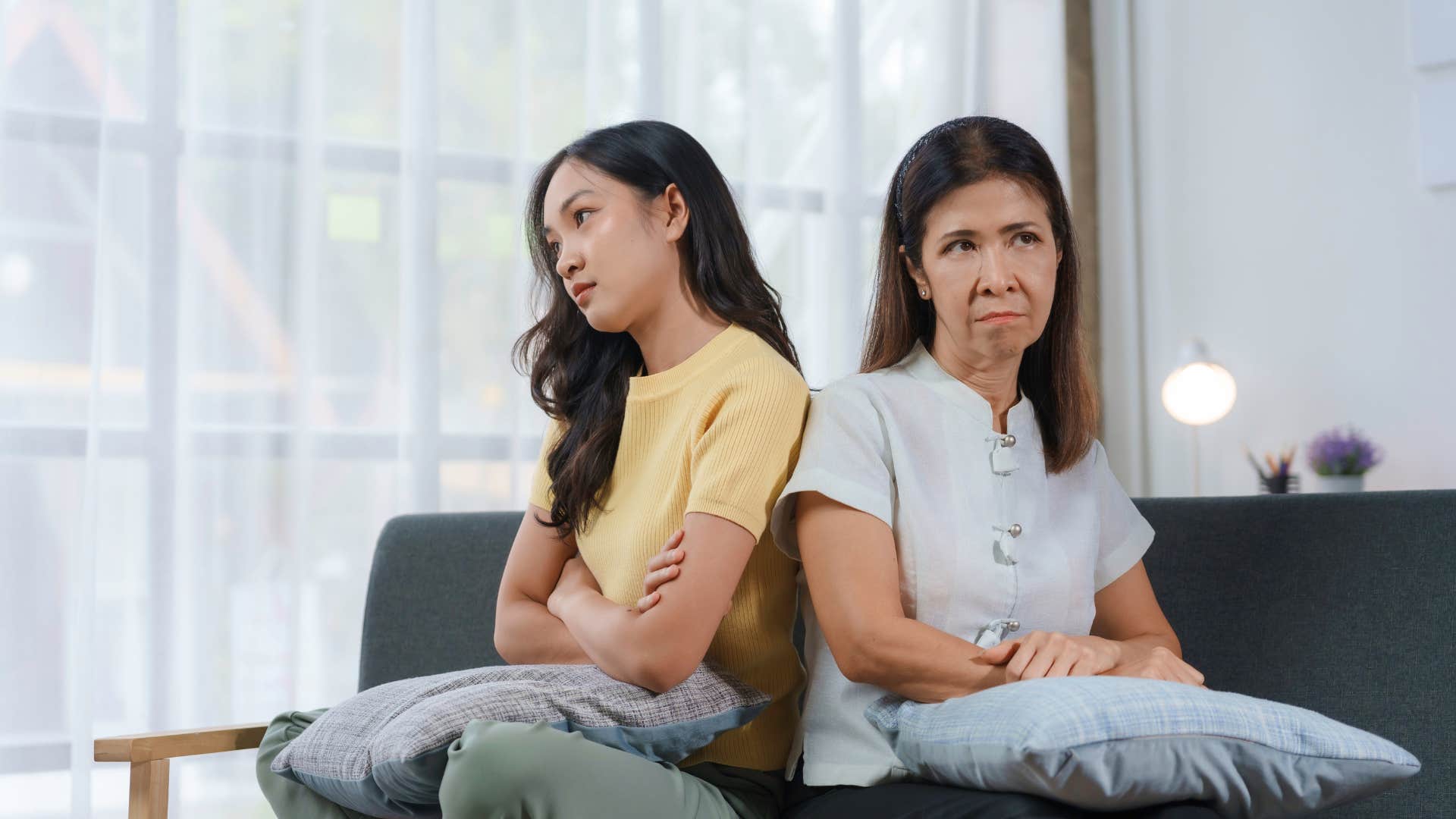 young woman and an older woman are sitting with their arms crossed not looking at each other after an argument