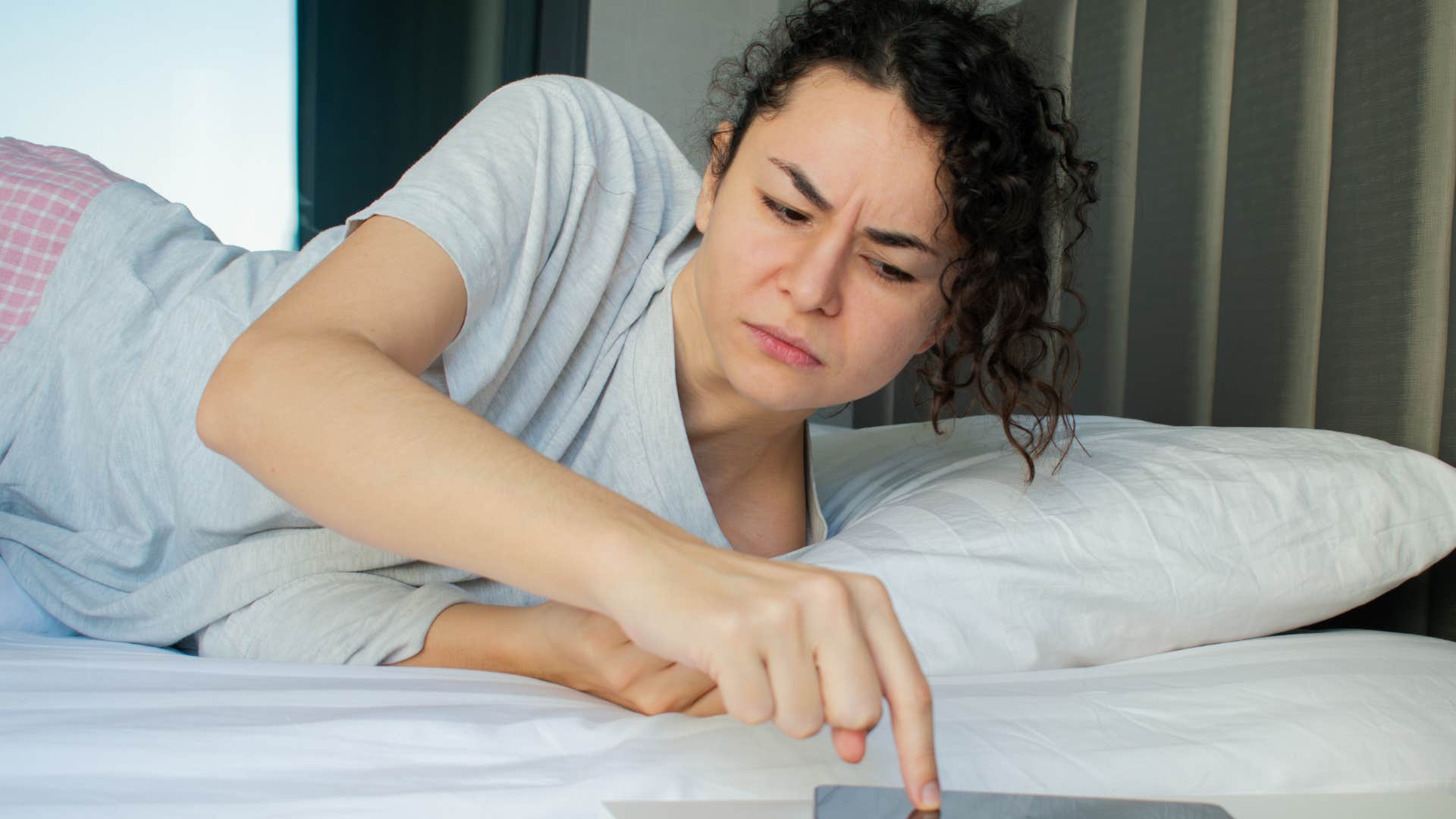 Woman waking up to an obnoxious alarm in bed.