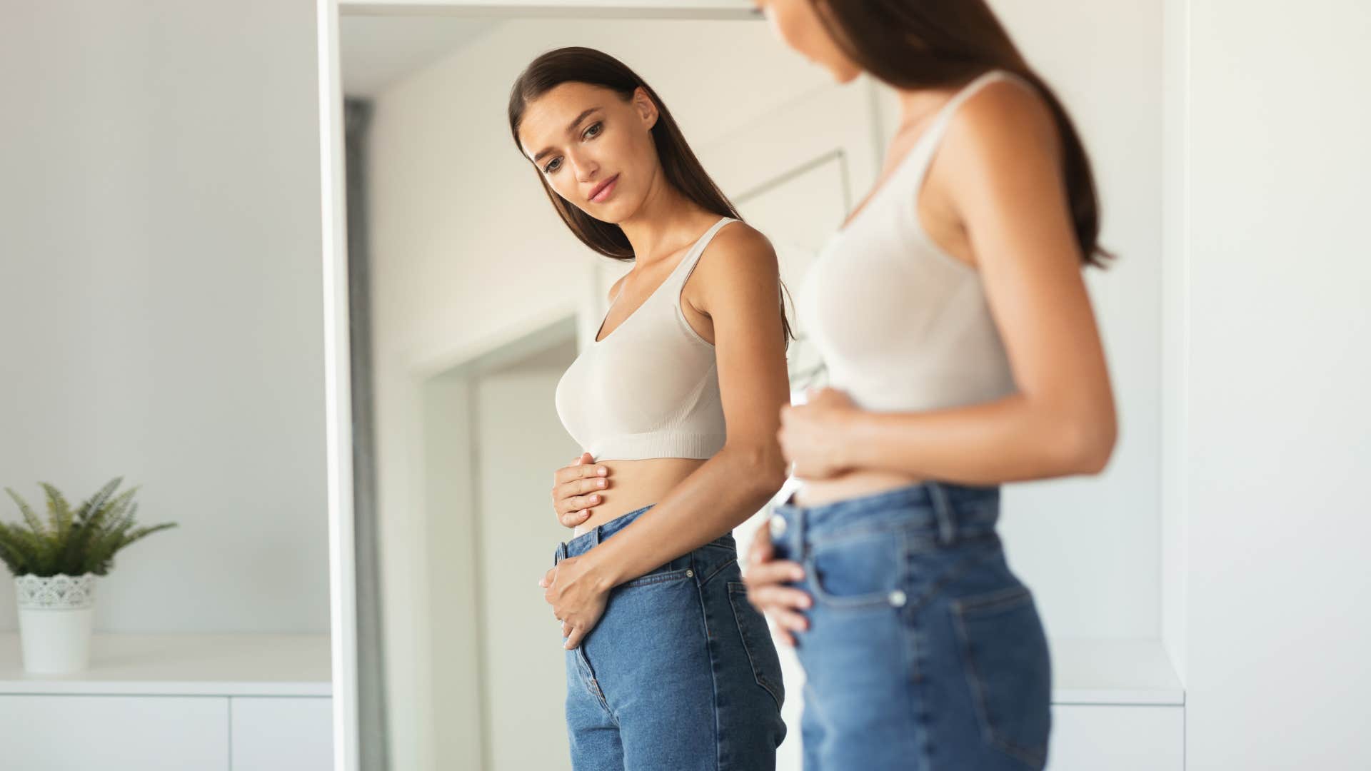 woman looking at her body in the mirror
