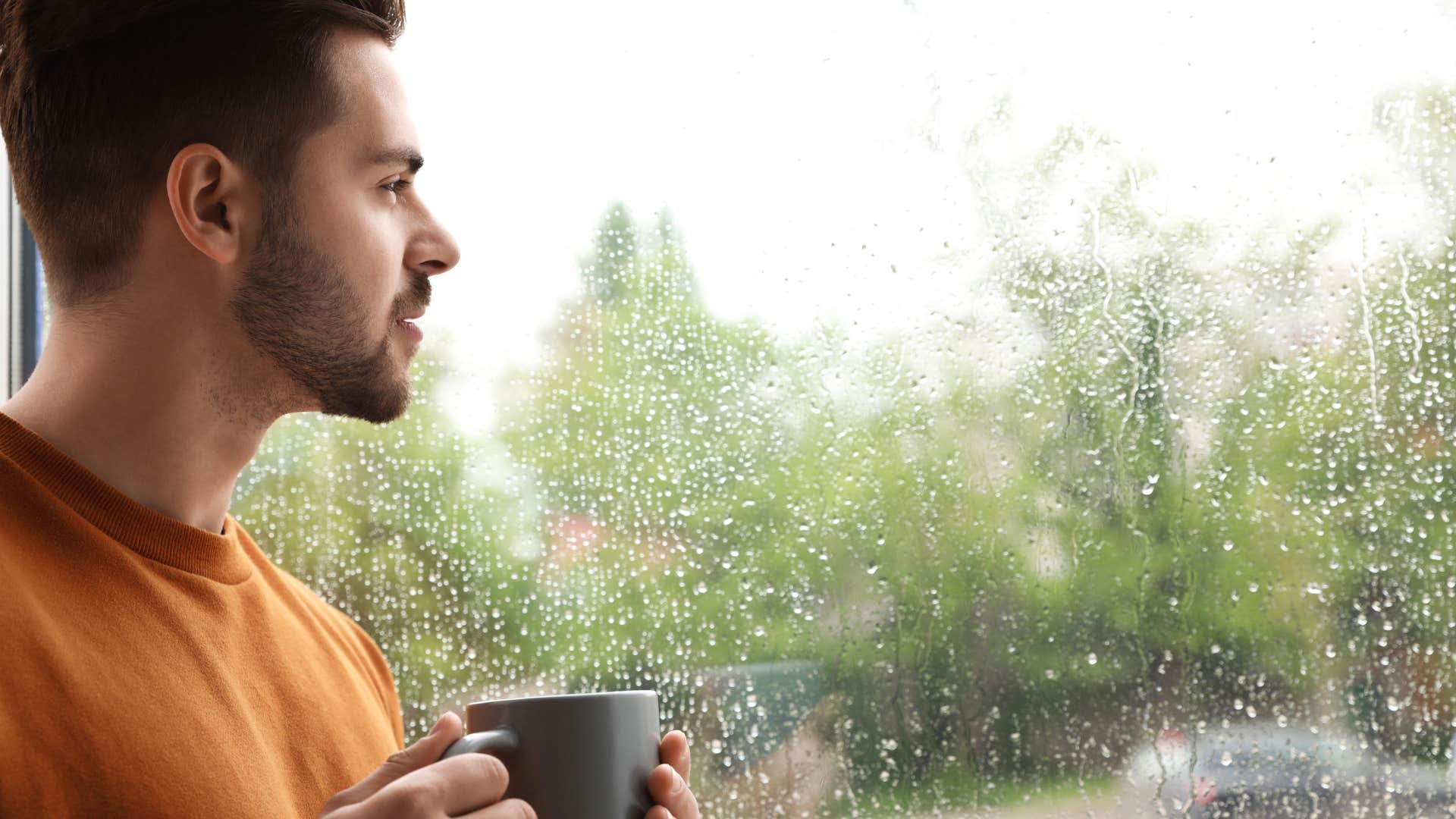 man looking out window at rain