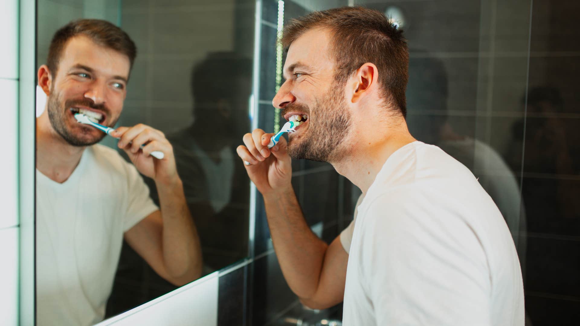 man brushing his teeth in bathroom mirror