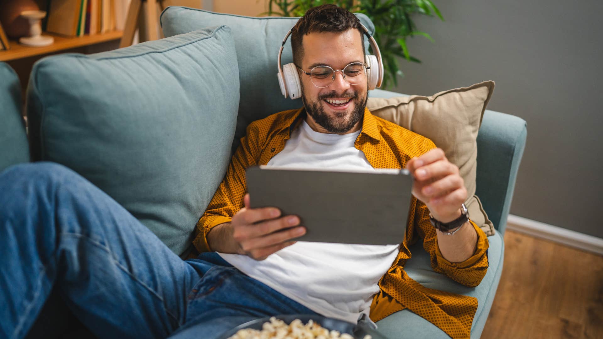 man watching movie on tablet with headphones and bowl of popcorn
