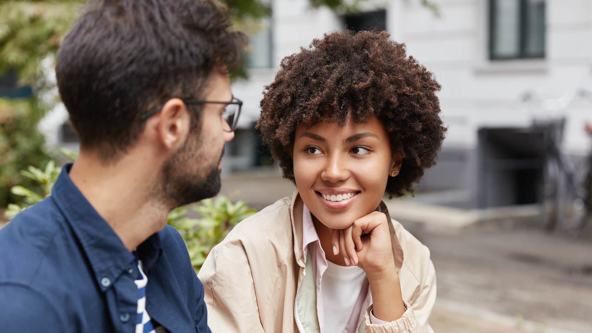 woman in light brown jacket becomes more curious about his love life as she smiles