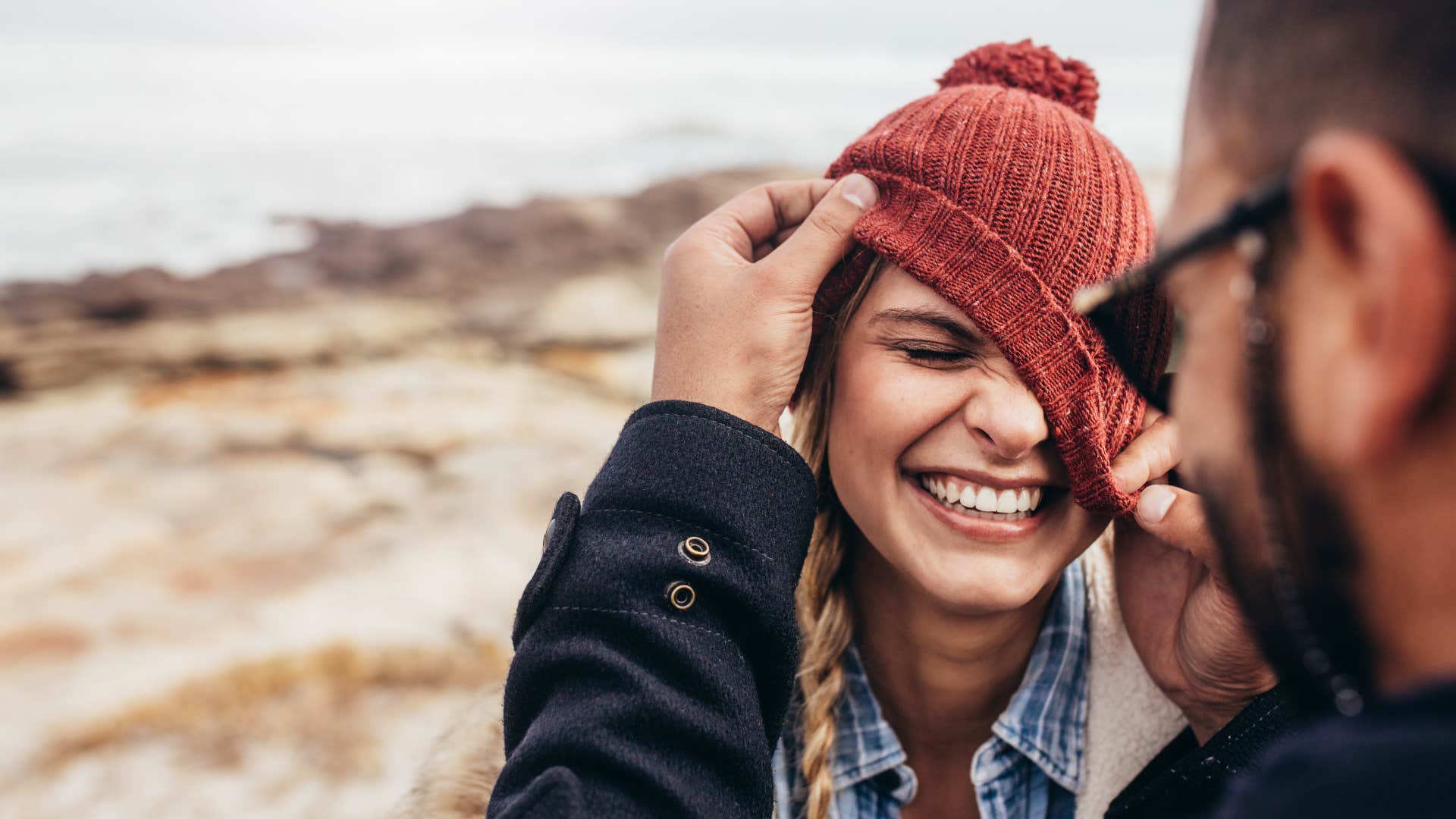 woman in red hat laughs more around him as man tries to fix her hat