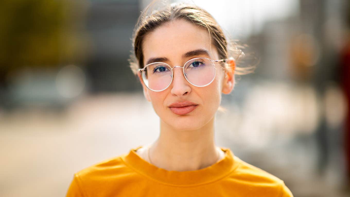 serious woman wearing glasses standing outside thinking