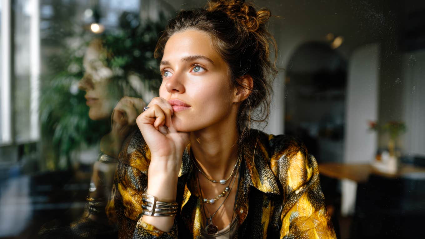 A woman bathed in soft morning light looks out a window with quiet strength, capturing the bittersweet beauty of learning what real love feels like beyond the fairy tale.