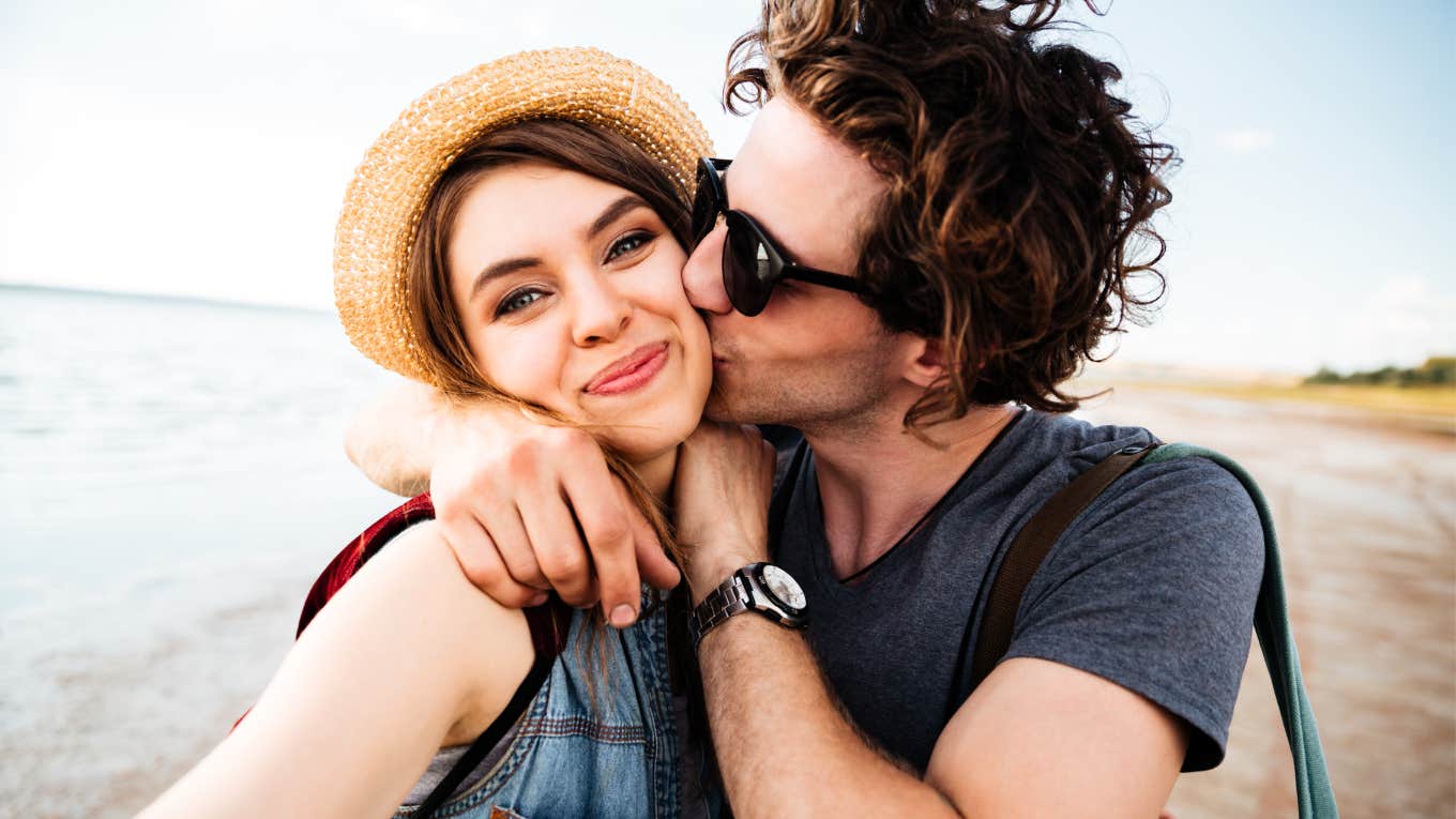 Playful couple on the beach taking a selfie showing the art of fun and habits of couples who aren’t boring and blah