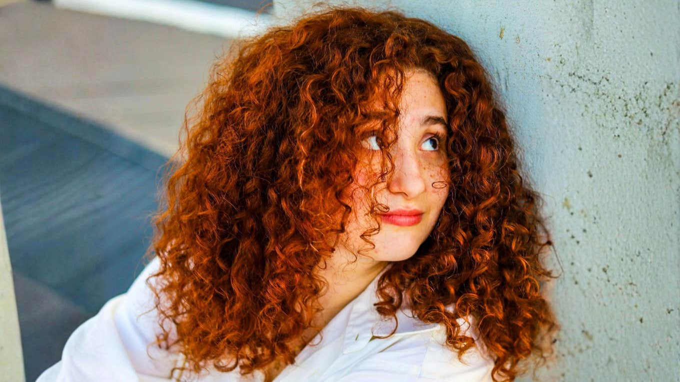 Confident, composed woman with red curly hair outdoors showing the art of emotional command and habits of people who stay present in tough times.