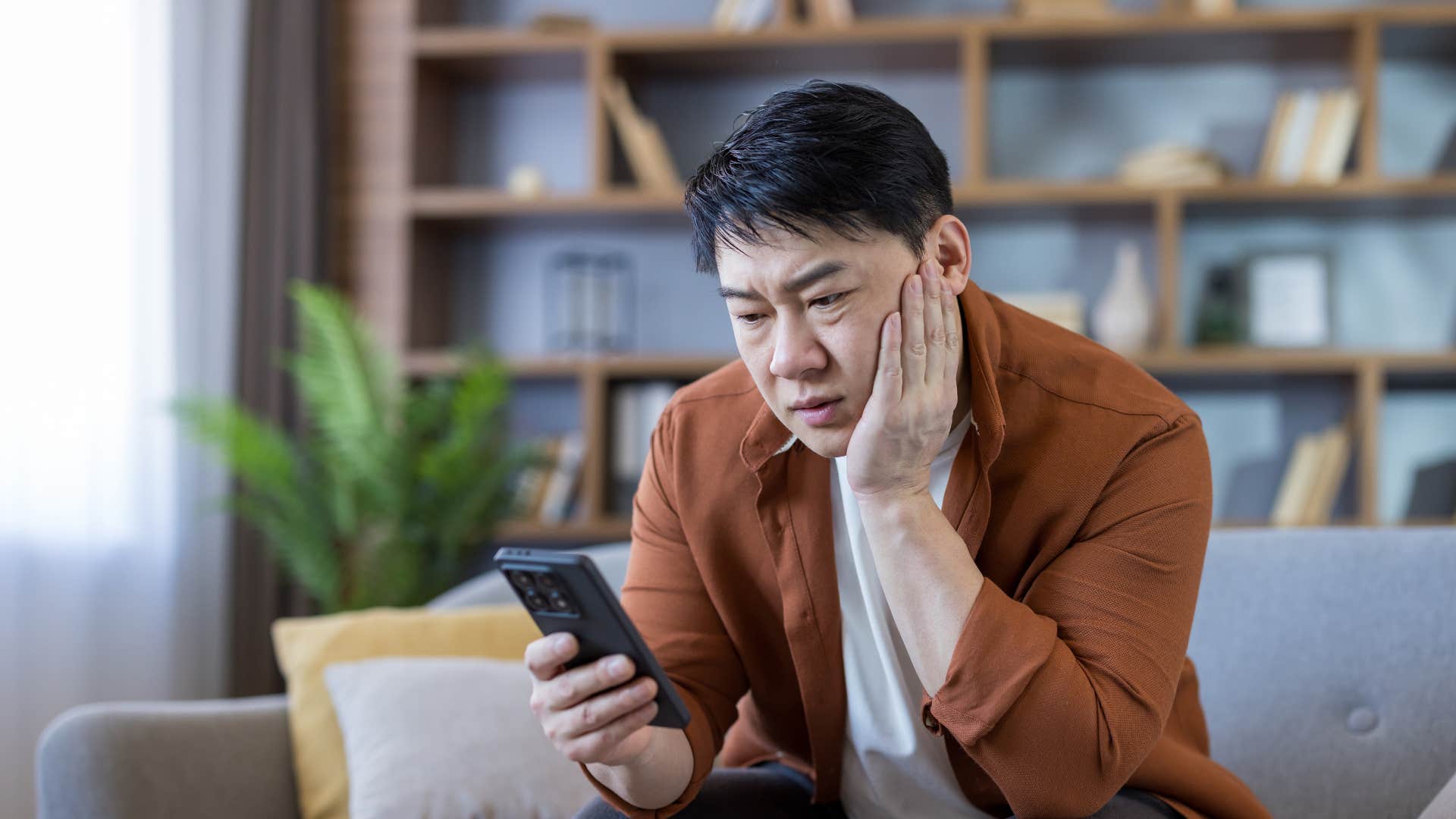 man in brown jacket replaying family videos constantly as he looks sad
