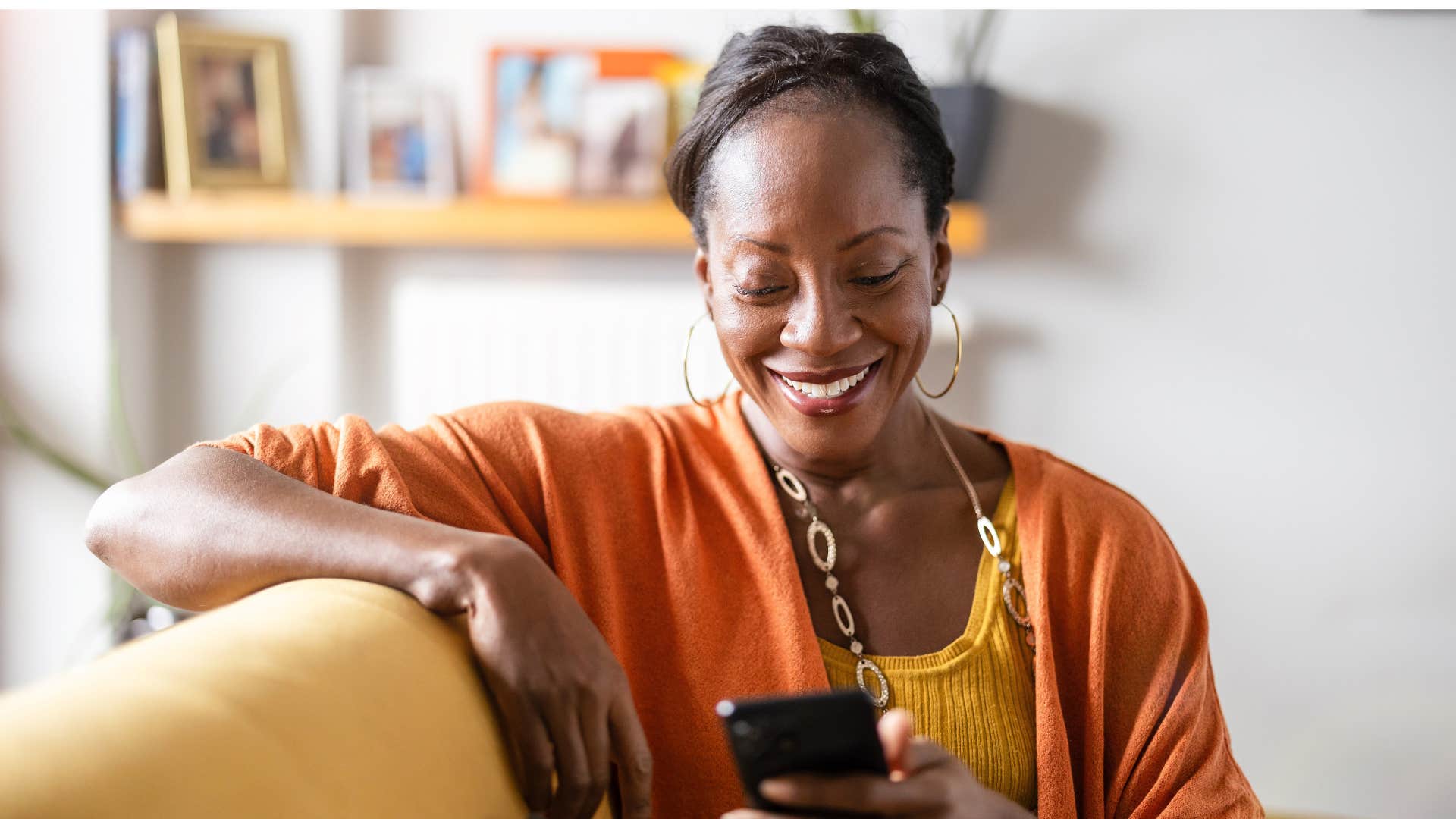 woman in orange cardigan watches too much tv as she scrolls endlessly on phone while smiling