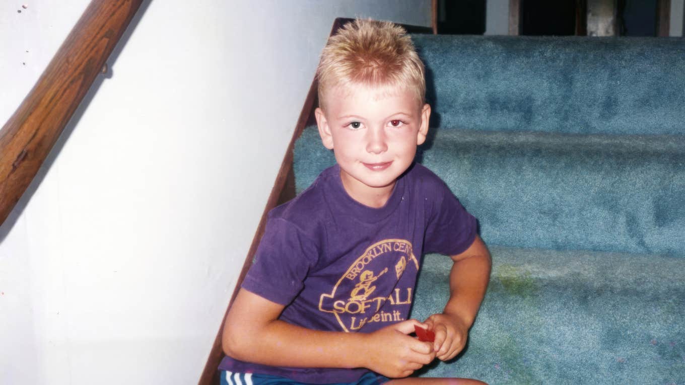Young 90s kid sitting, playing on blue carpeted stairs, capturing the forgotten life lessons that shaped stronger generations.