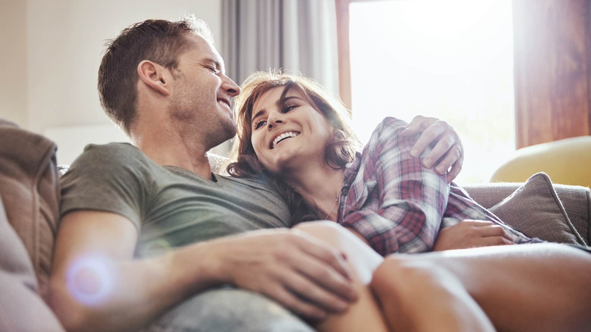 husband and wife smiling together on couch cuddling
