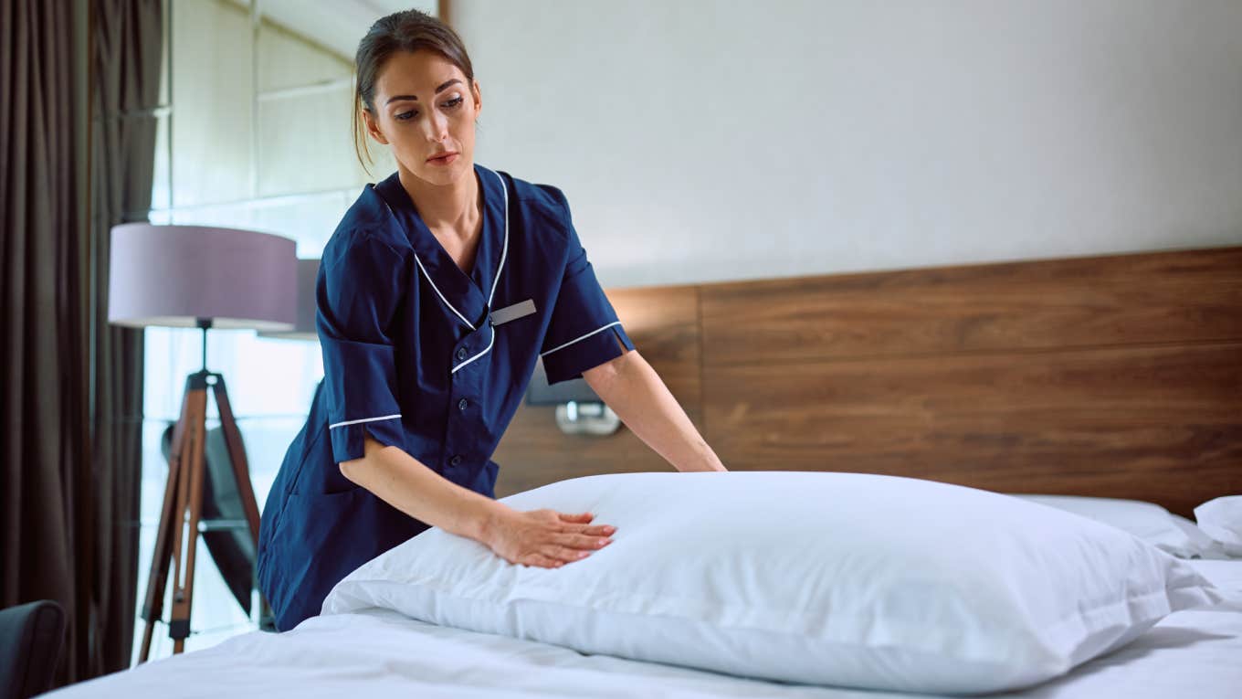 young female housekeeper at hotel making bed