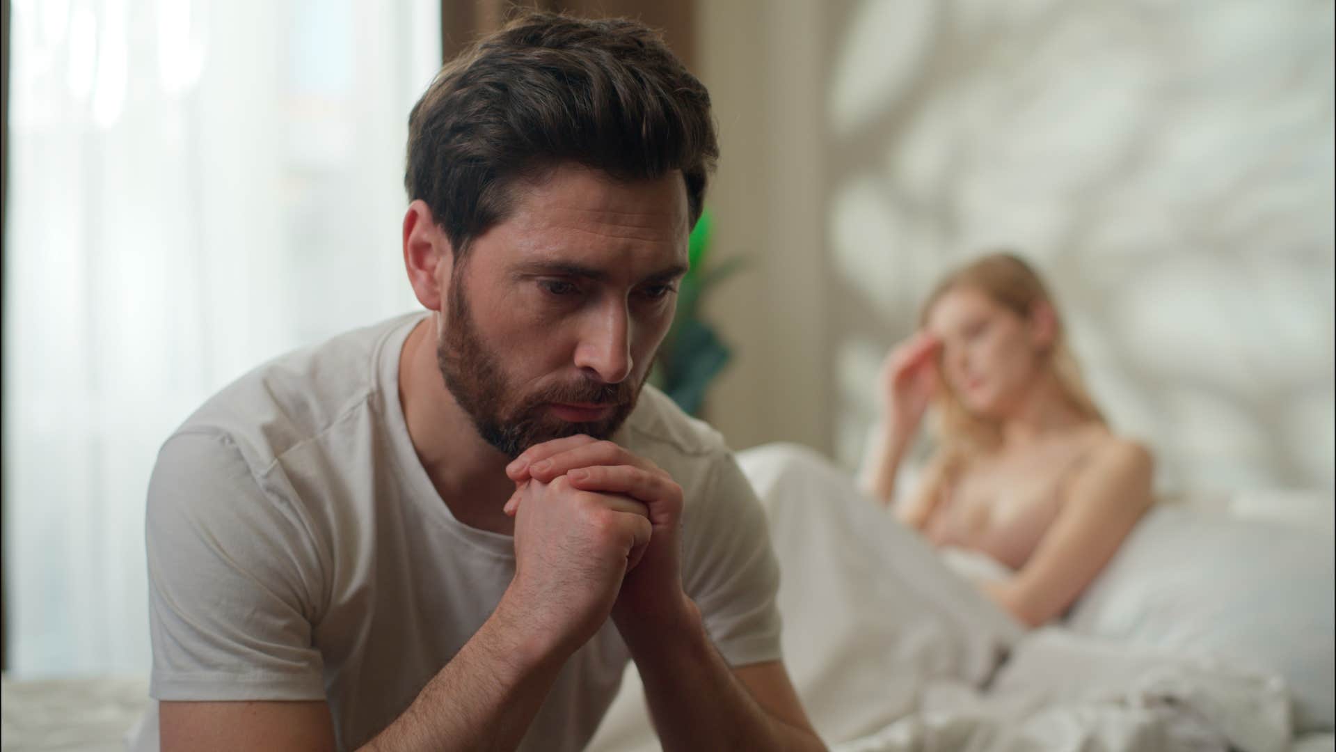 distressed man sitting away from wife in bed