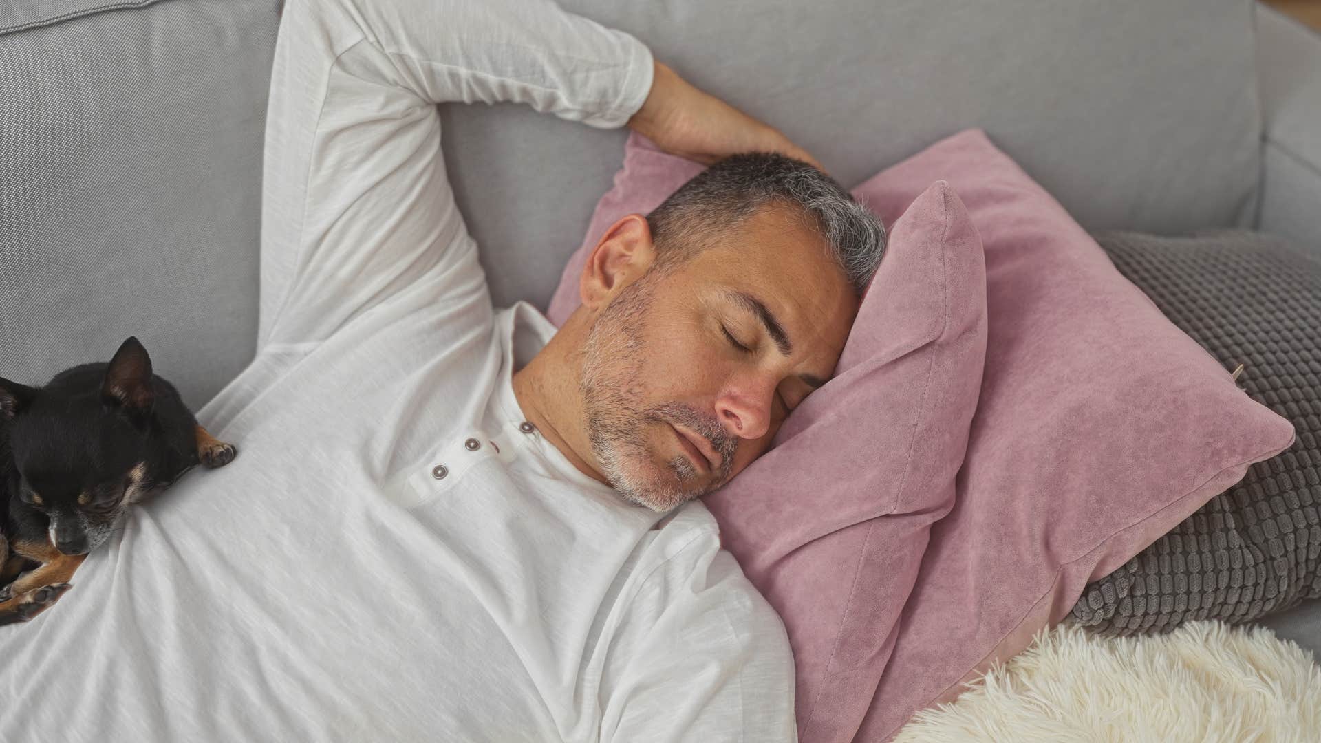 man with different bedtime preferences sleeping on the couch with dog