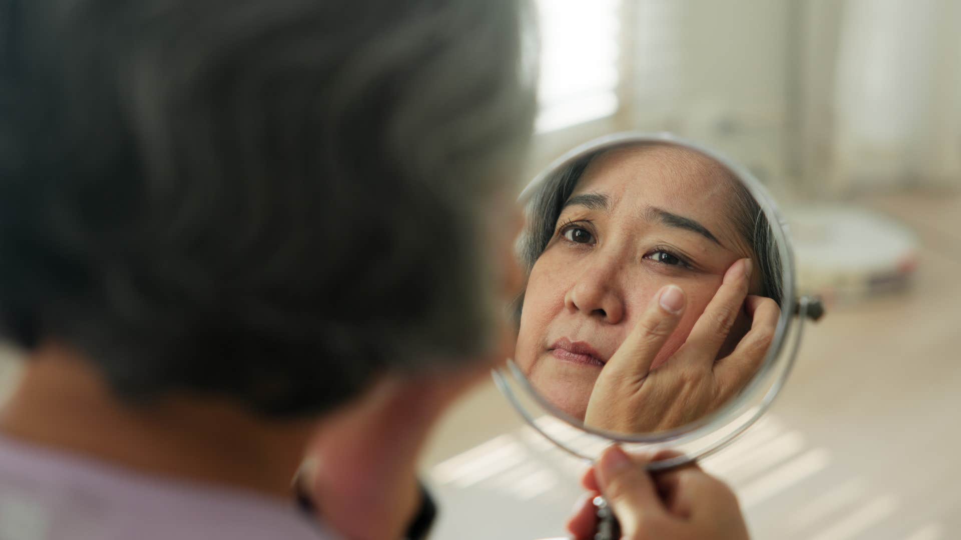 Woman who fears judgment from others looking in a mirror.