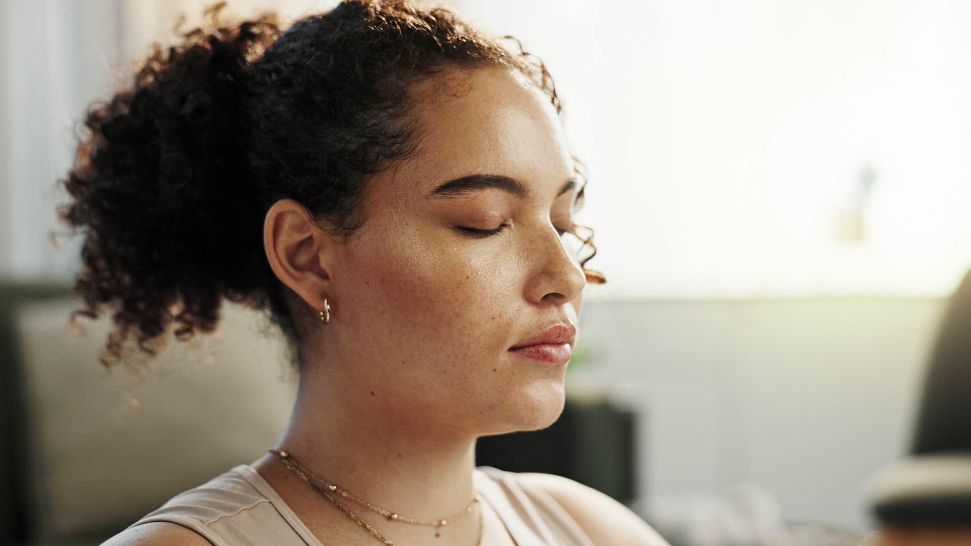 Woman meditating at home with stacks of incense and crystals.