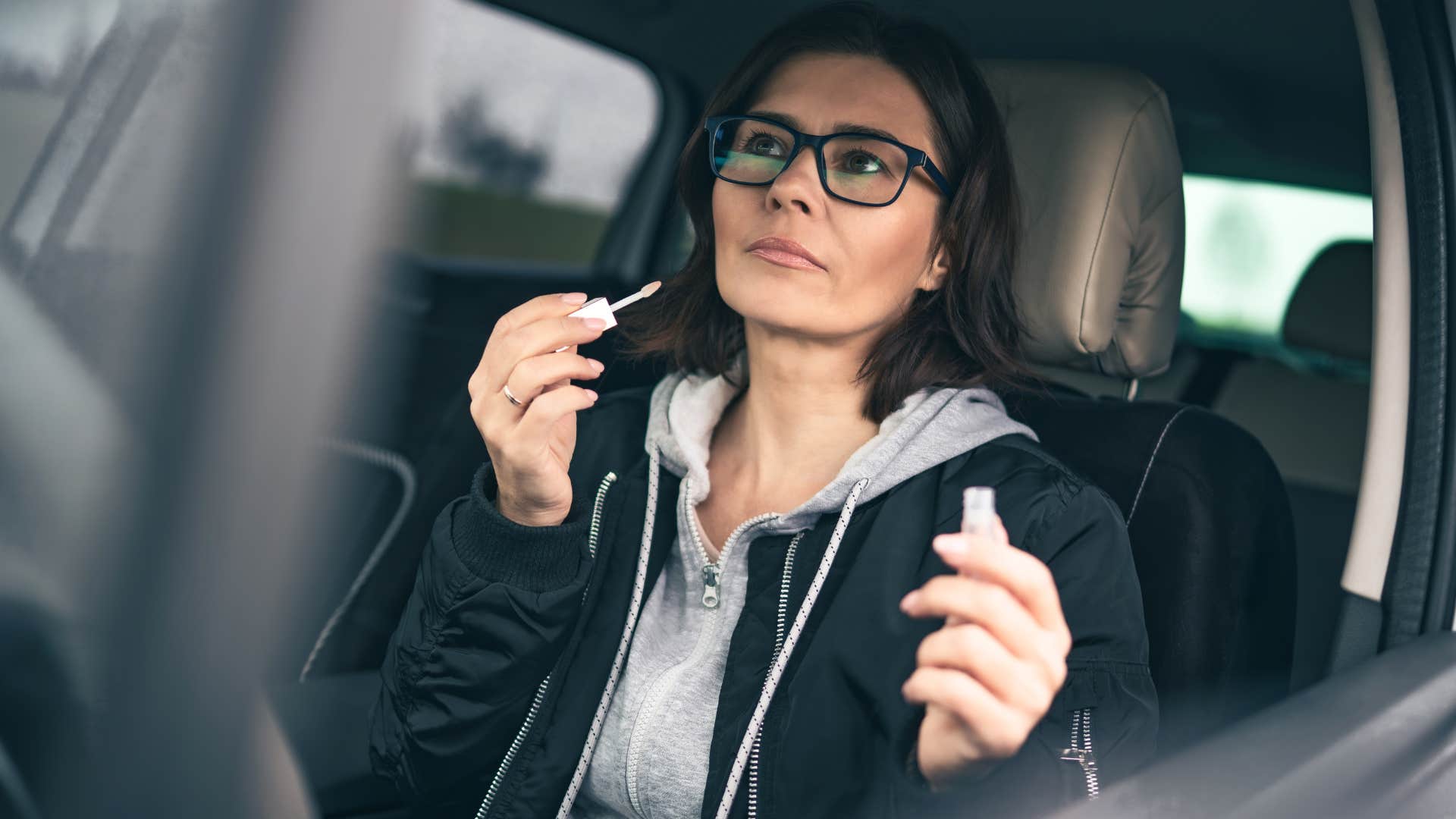 woman whose glove box is full of junk doing her makeup in the car