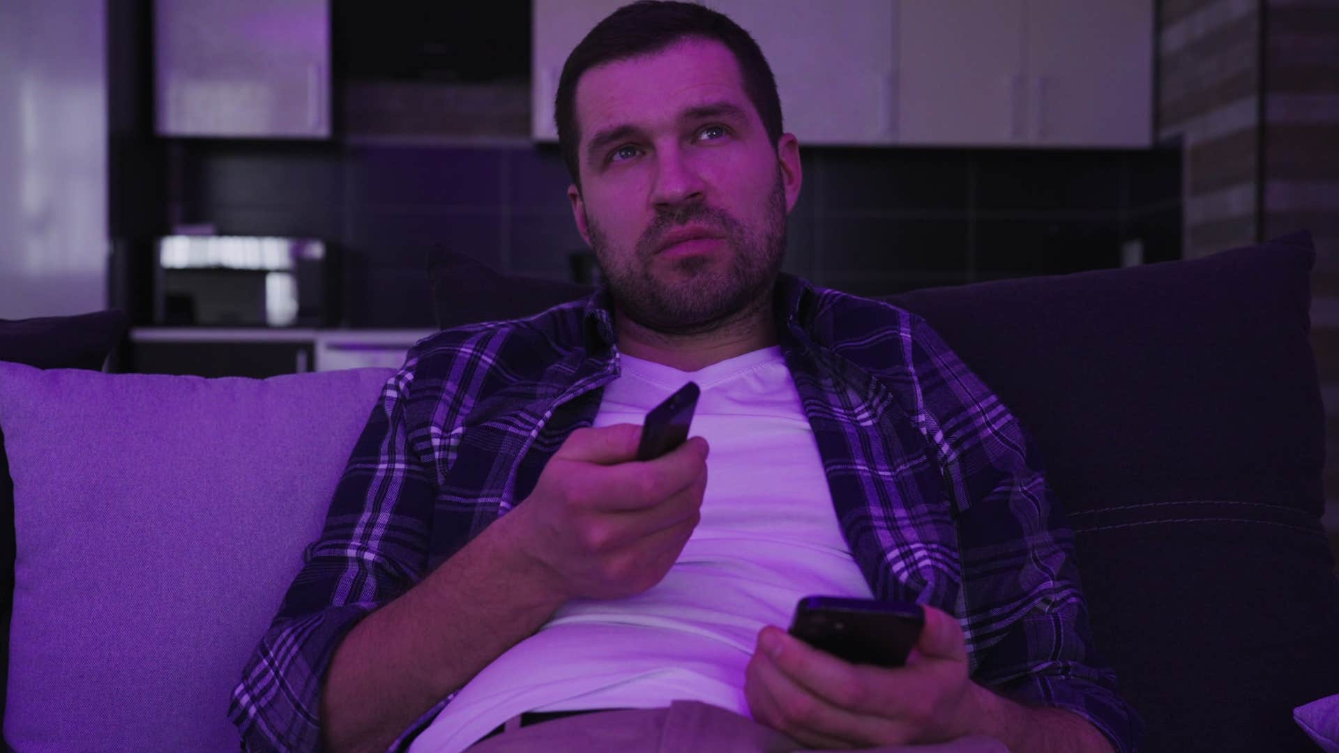 Man watching TV near an untouched self-help book.
