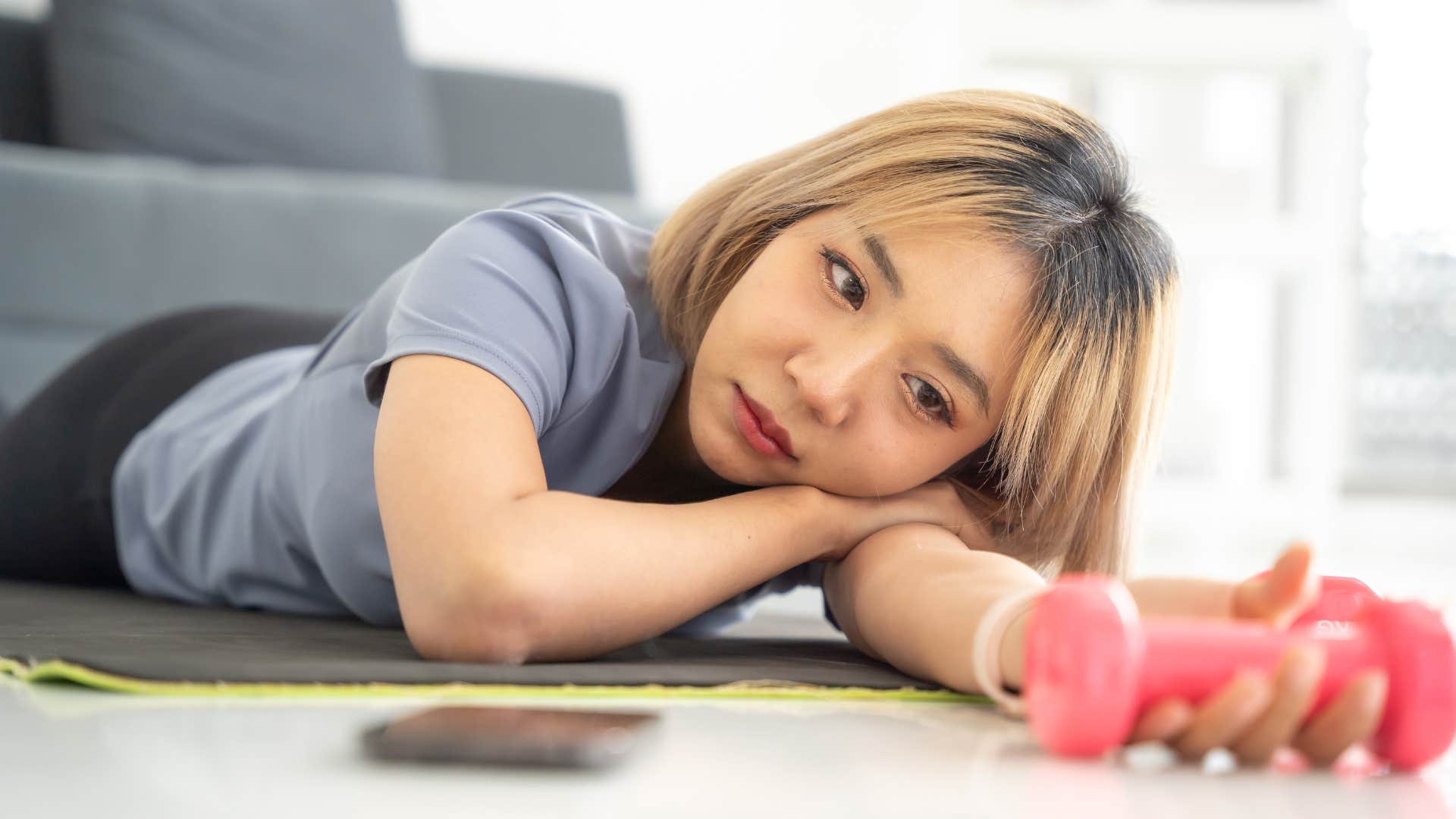 Woman sitting with unused workout equipment at home.