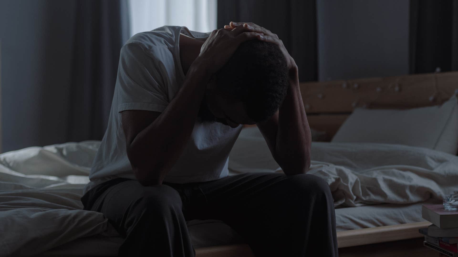 stressed man sitting in dark room with the blinds closed