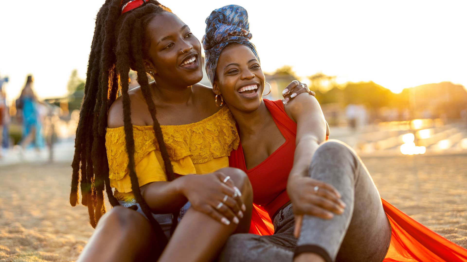 two women hugging each other and sitting on beach