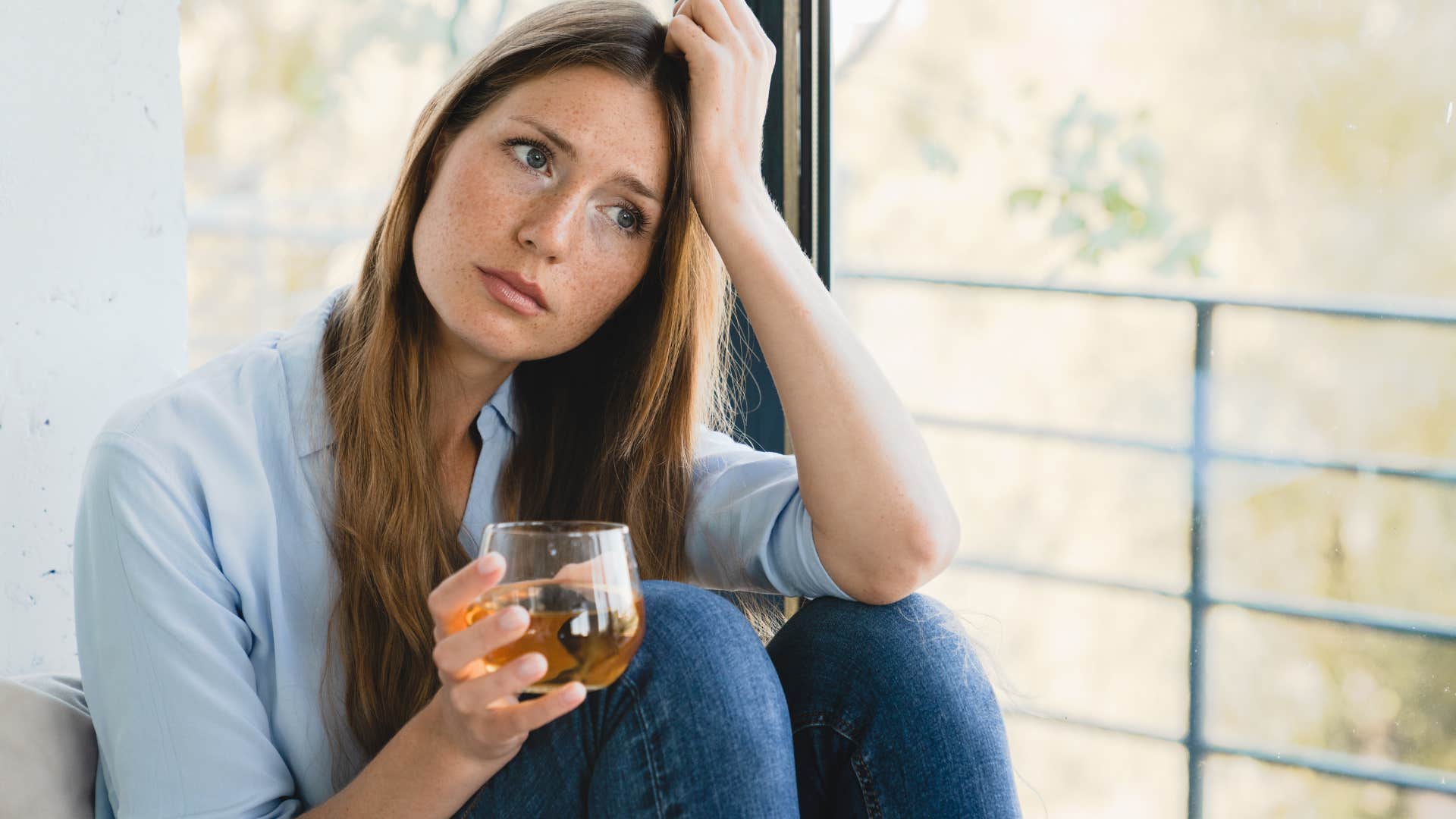 stressed woman sitting by window holding cup of tea