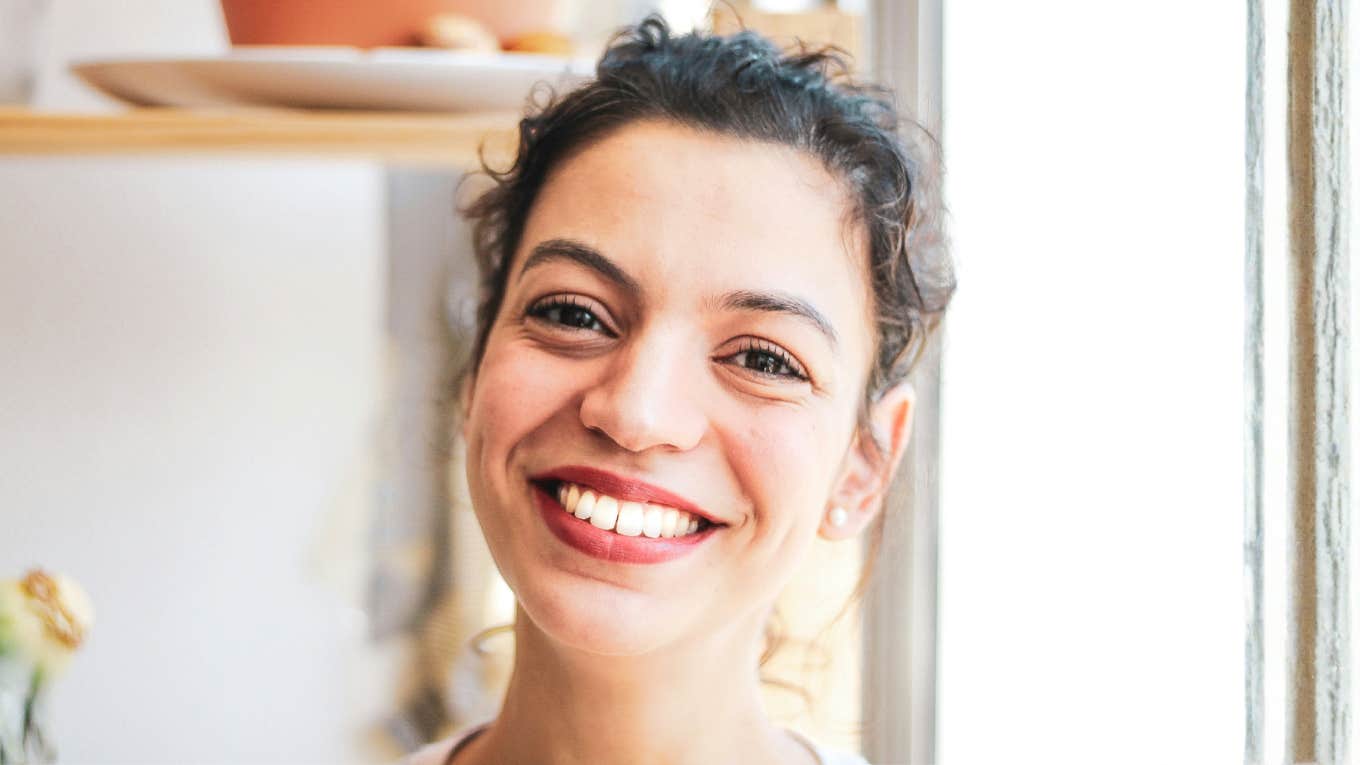 Happy woman standing in her kitchen, embodying the calm, magical energy of an easy bay leaf manifestation ritual.