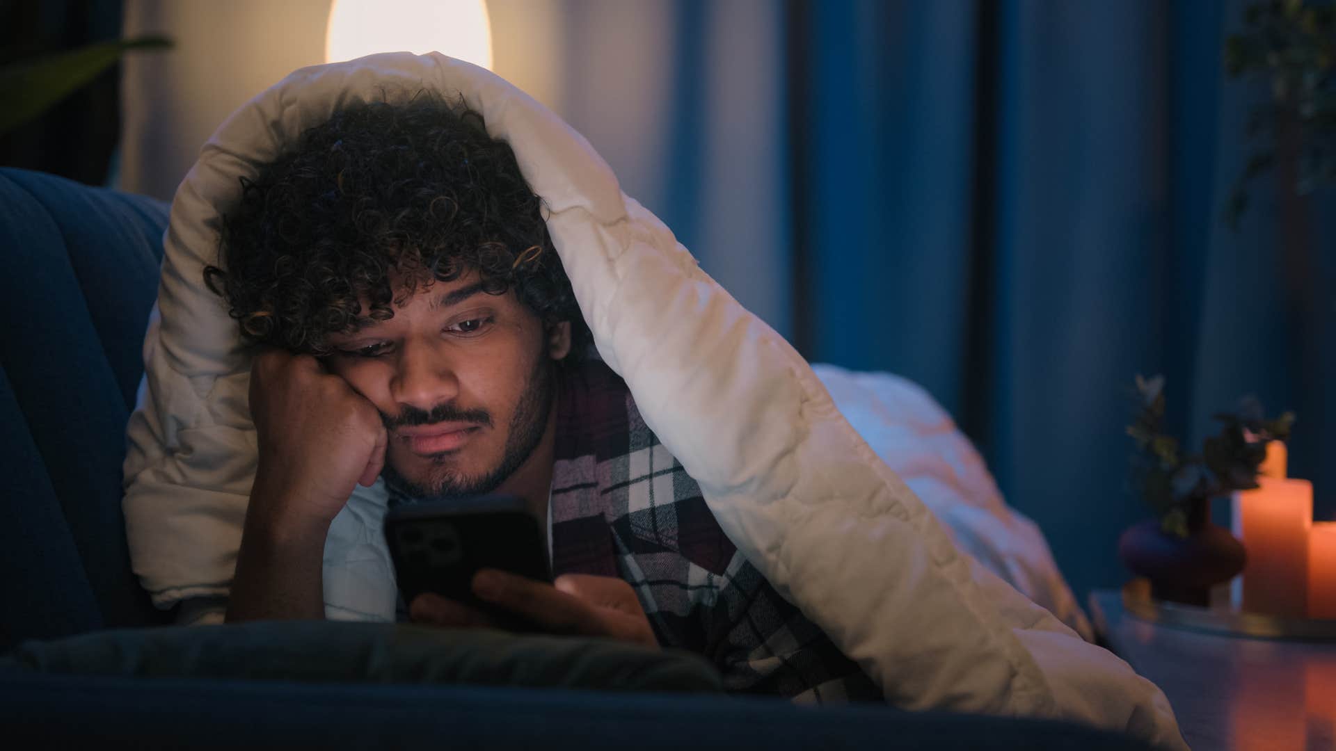 man under blanket looking bored as he texts less frequently 