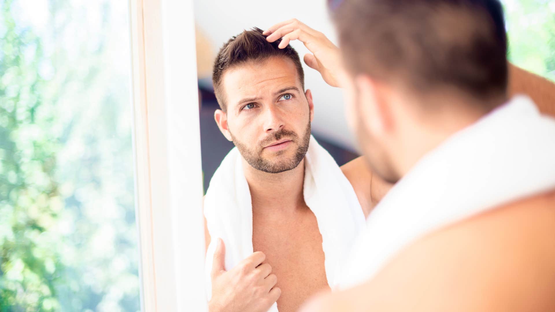 man looking at his hair in the mirror