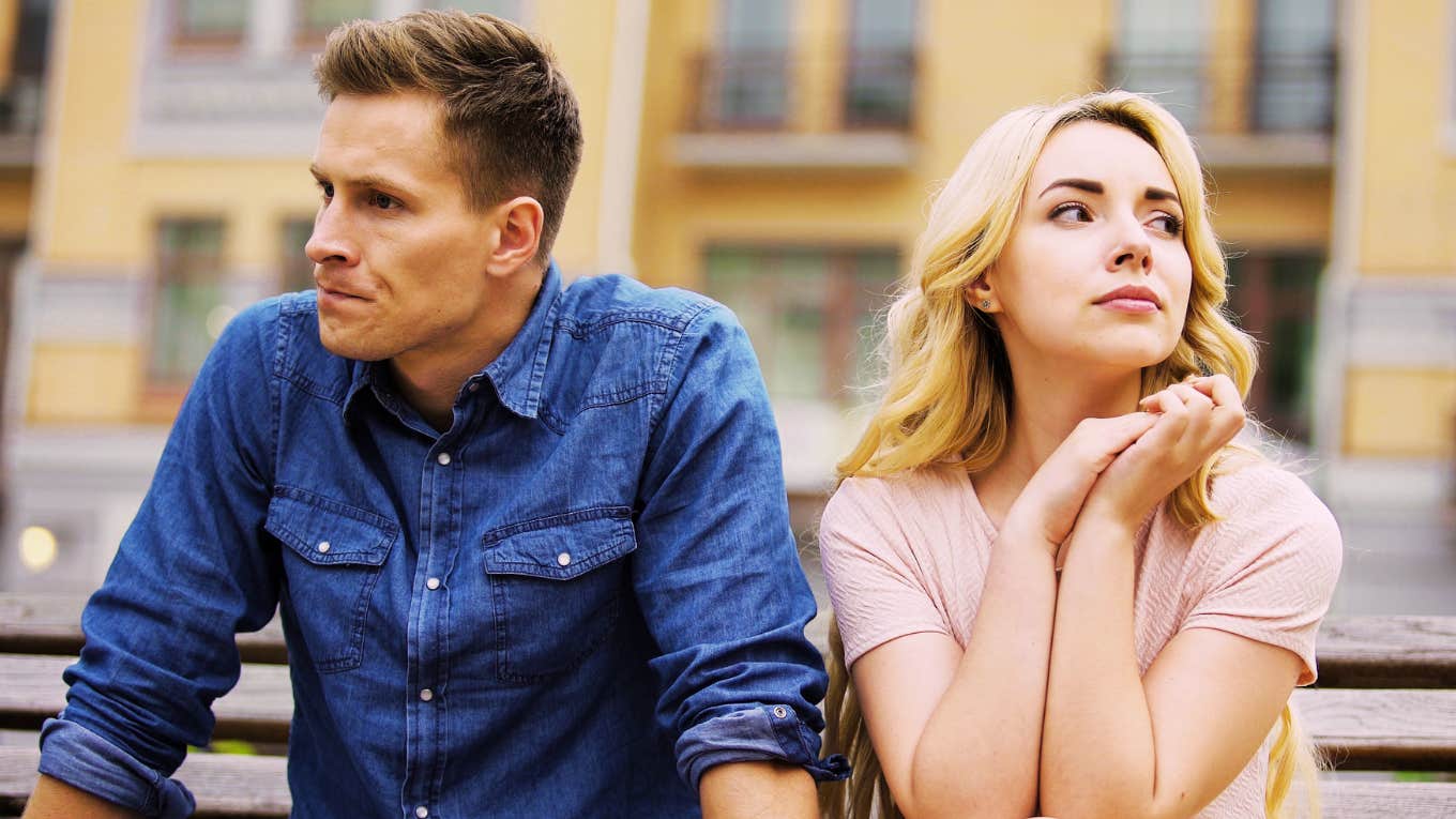 Upset couple sitting on a bench, with the man looking frustrated and the woman crying, illustrating the most dangerous relationship emotion and how it begins to spread between partners.