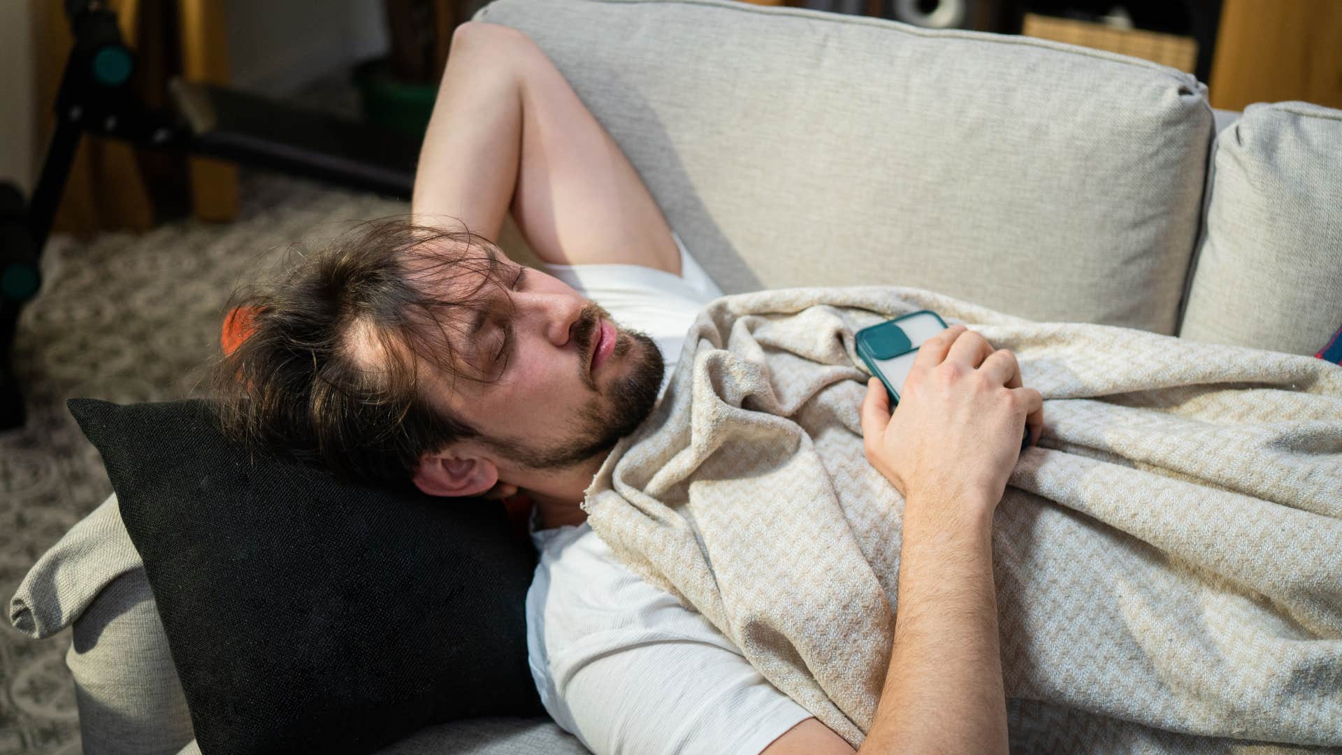 man sleeping on couch looking like he hasnt showered