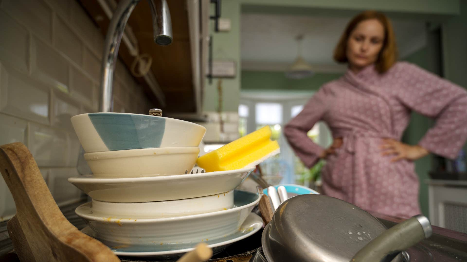 woman looking at sink full of piling up dishes