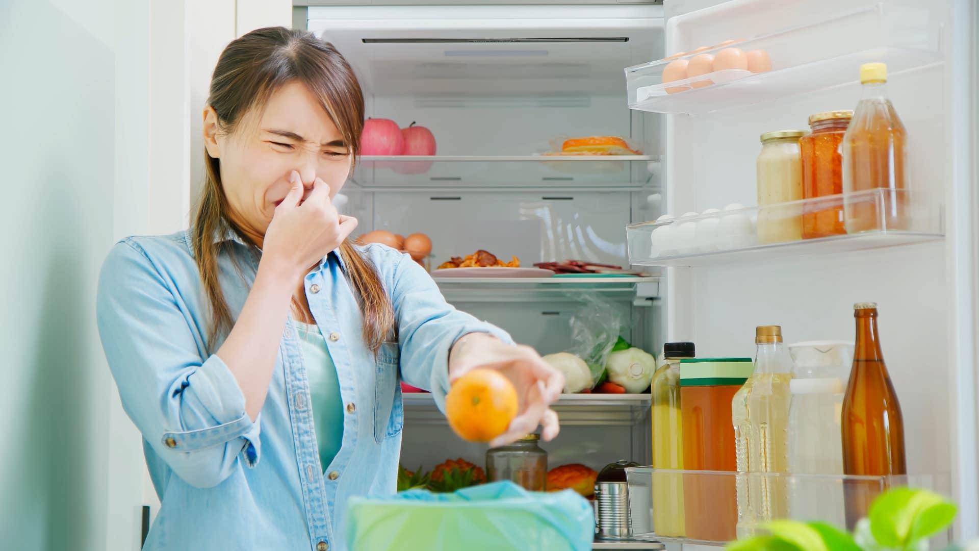 woman holding her nose cleaning expired food from fridge