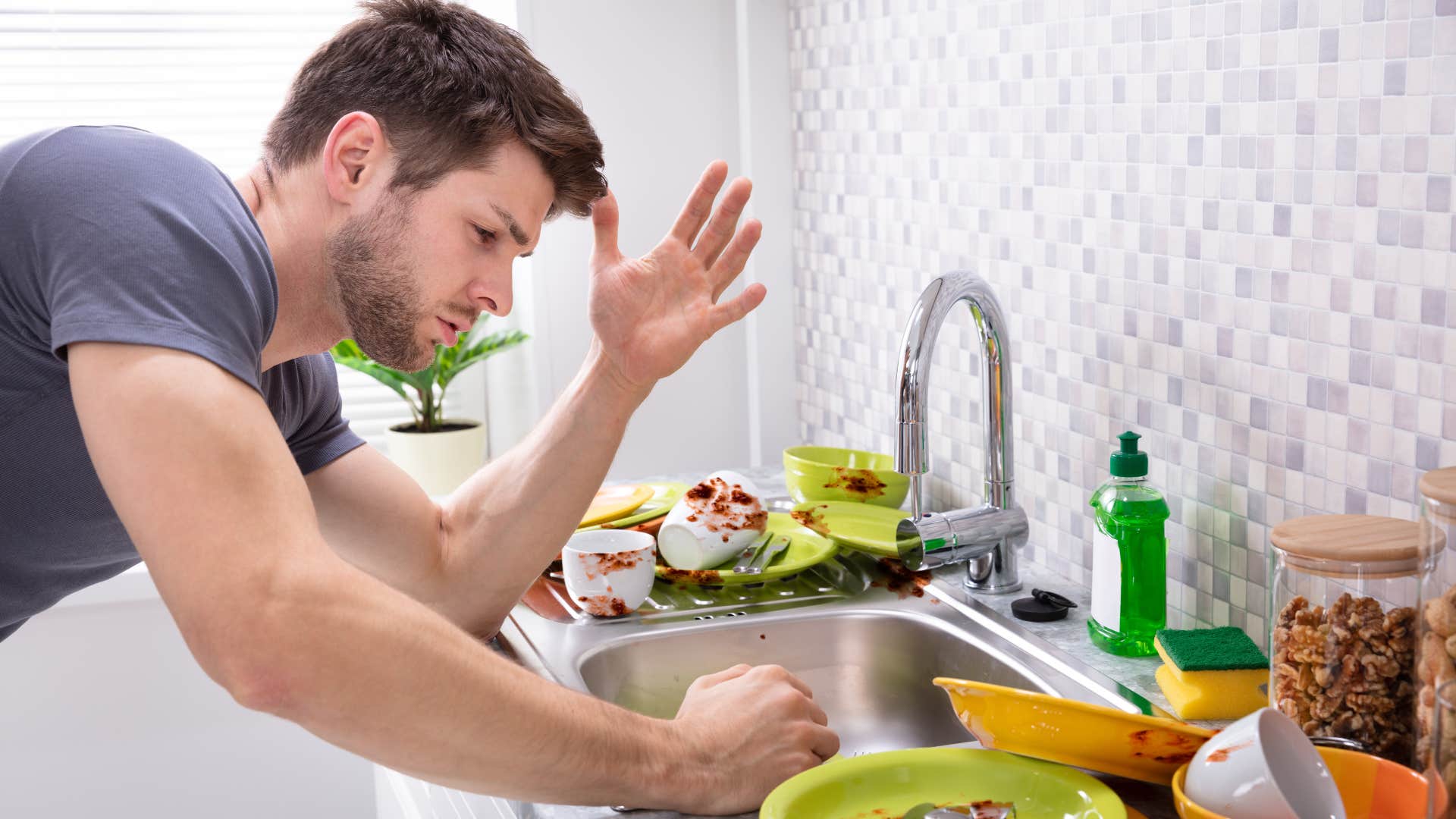 man stressed out over dirty dishes in his sink