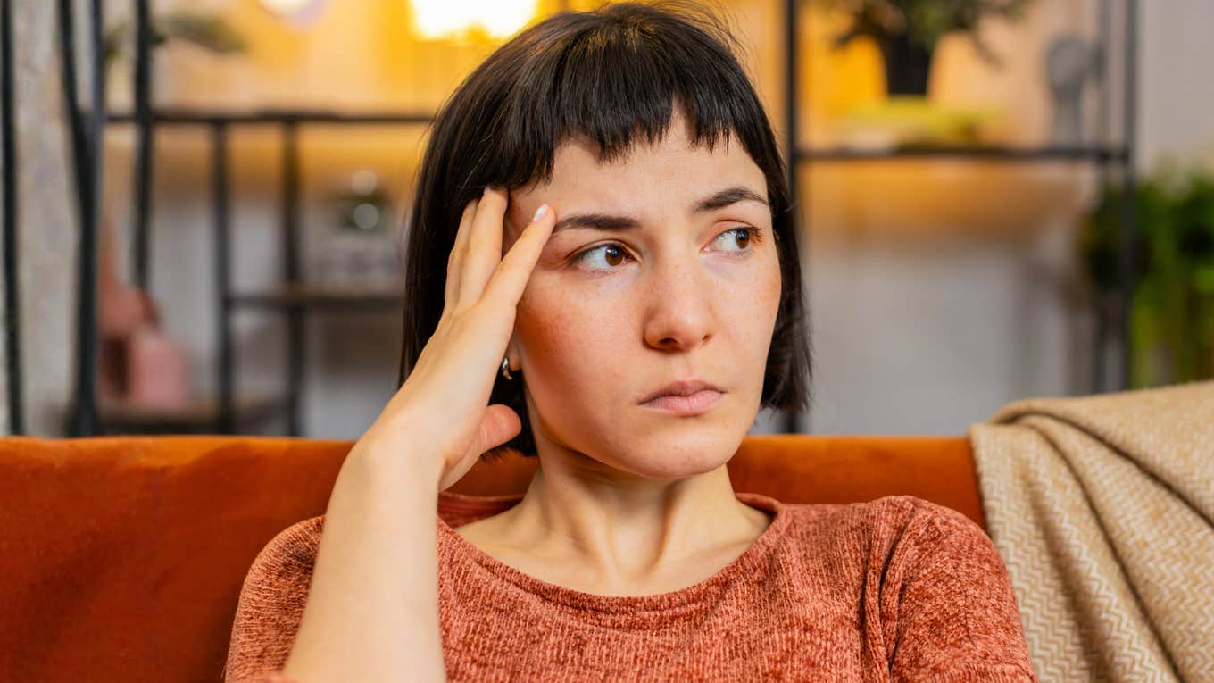 Upset woman with hand in her hair, deep in thought about her relationship, reflecting the painful truth of loving the idea of someone, not the person.