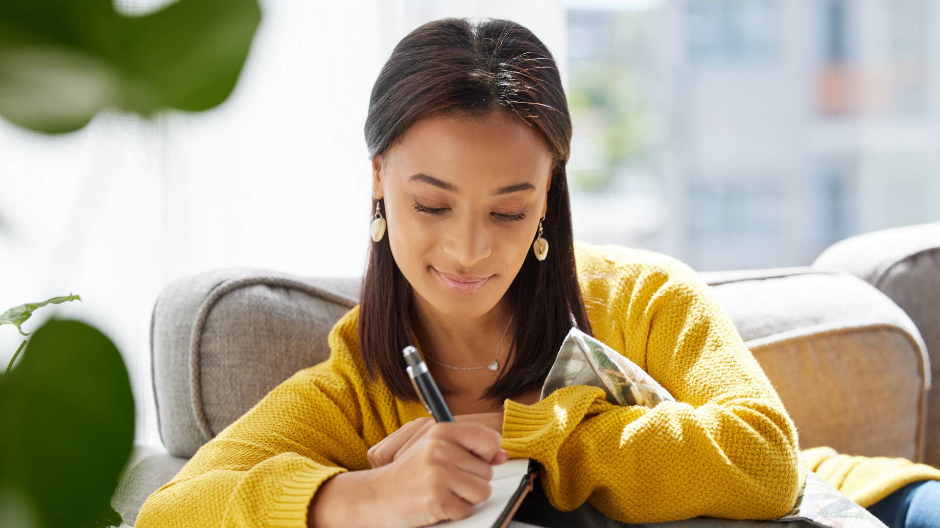 woman writing in self-help journal on couch