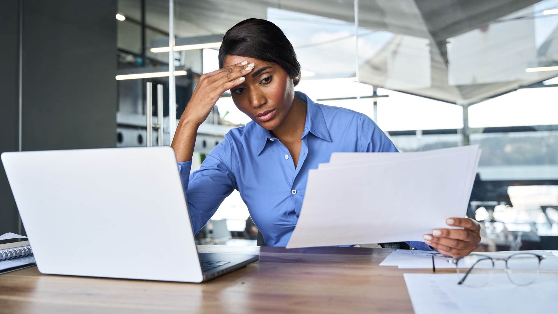 woman in blue shirt is chronically over scheduled as she looks stressed dealing with paperwork