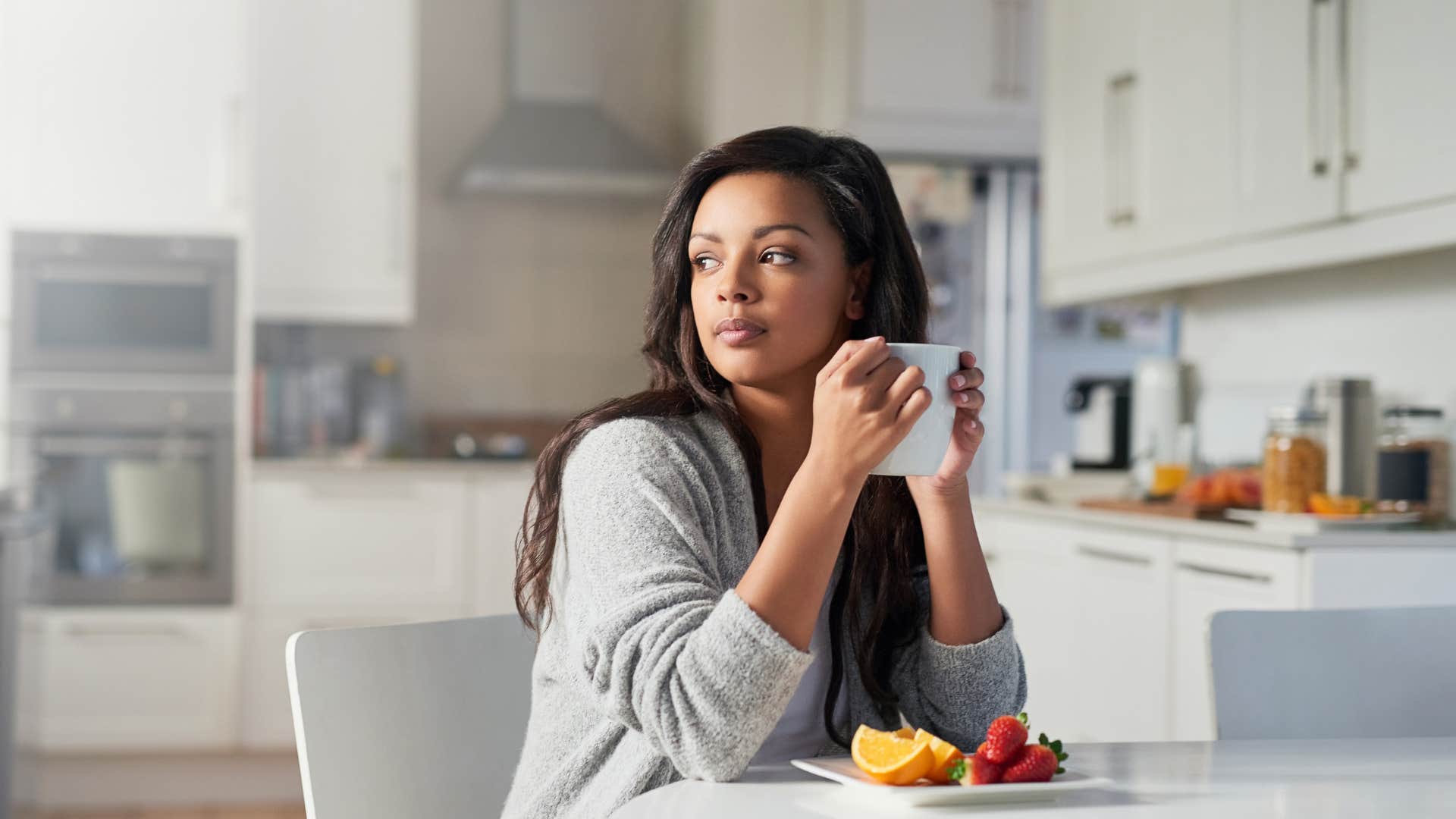 woman in gray cardigan with cup of coffee looking disconnected from their environment