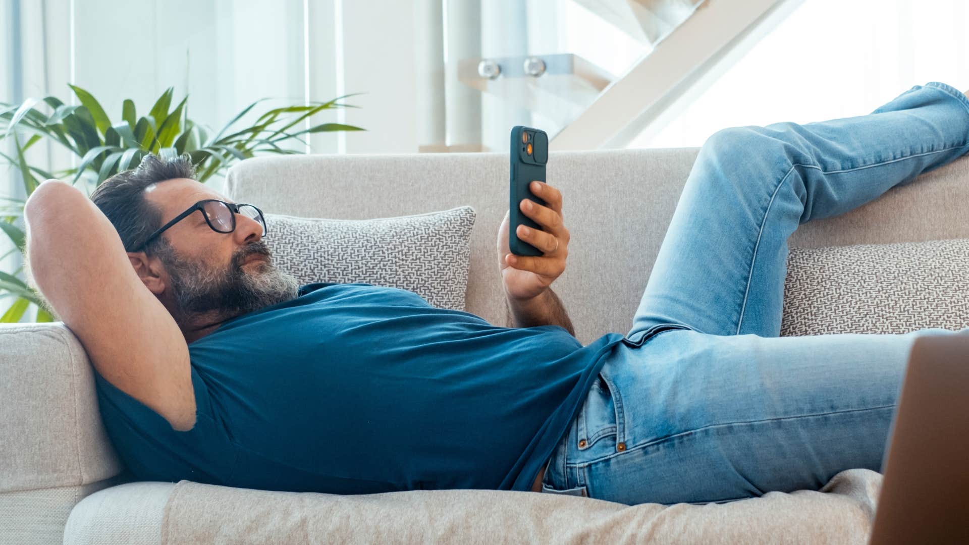 man on couch scrolling through phone lazily as he has a procrastination habit